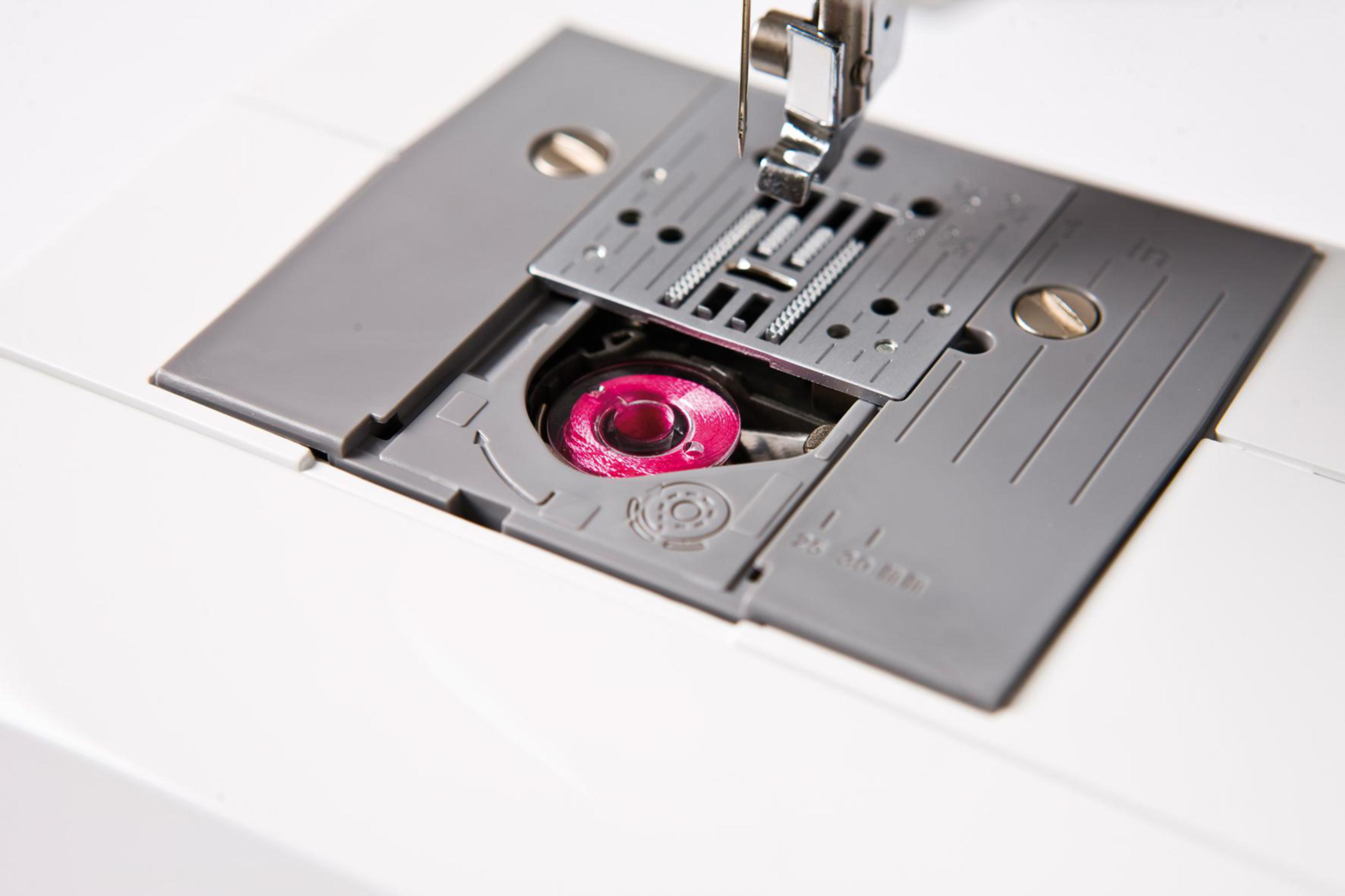 Nahaufnahme der Nähmaschine. Rosa Faden in der Spulenkapsel. Weiße Maschinenteile.
