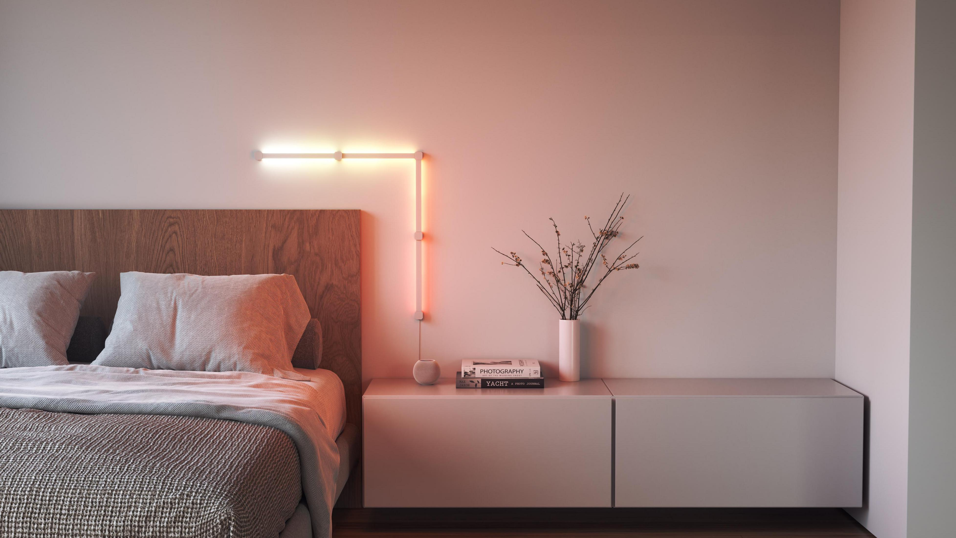 Una scena della camera da letto. Un letto con lenzuola bianche. Una luce a parete e un comodino.