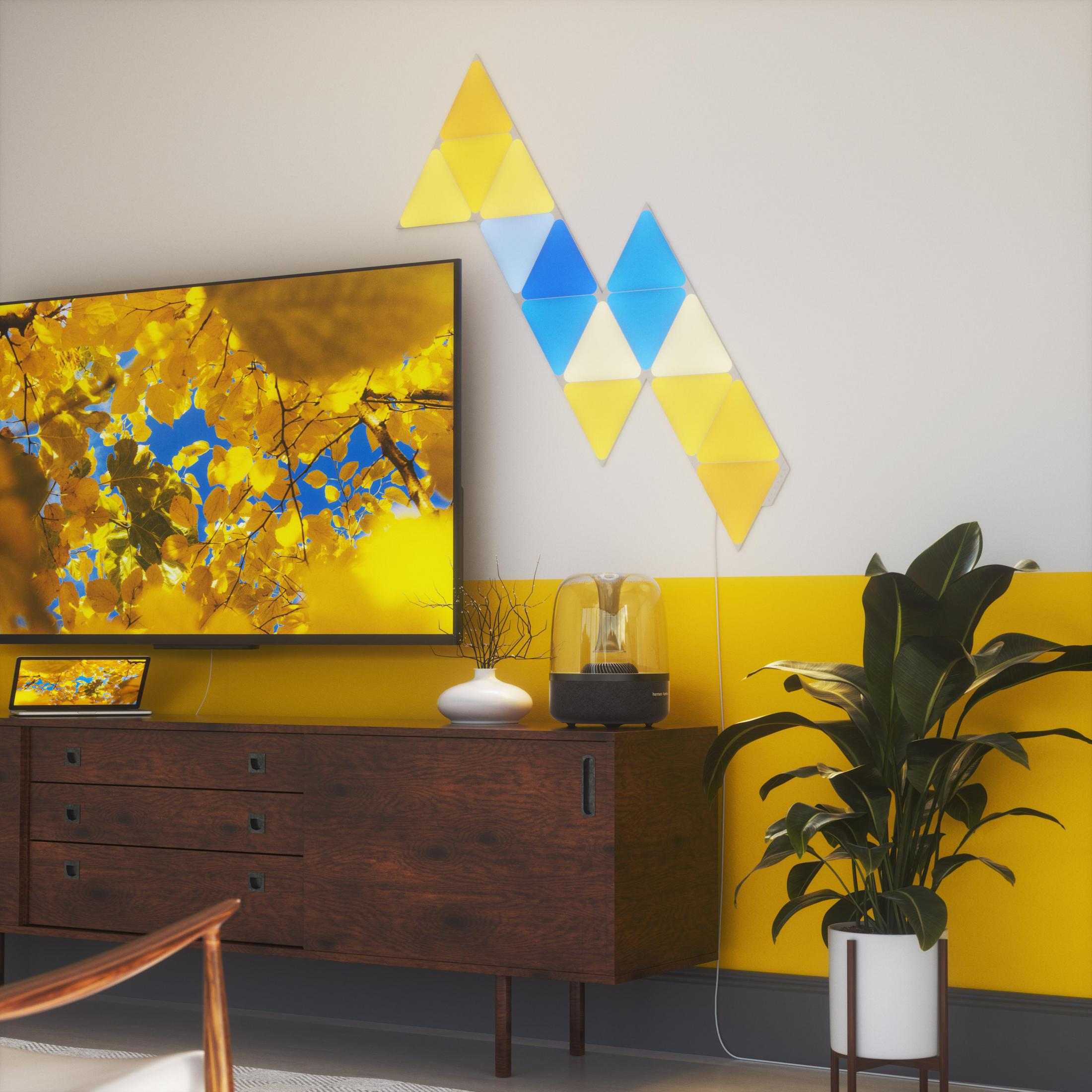 Eine Wand mit geometrischen Lichtern und einem Fernseher. Ein Schrank und eine Pflanze sind ebenfalls zu sehen.