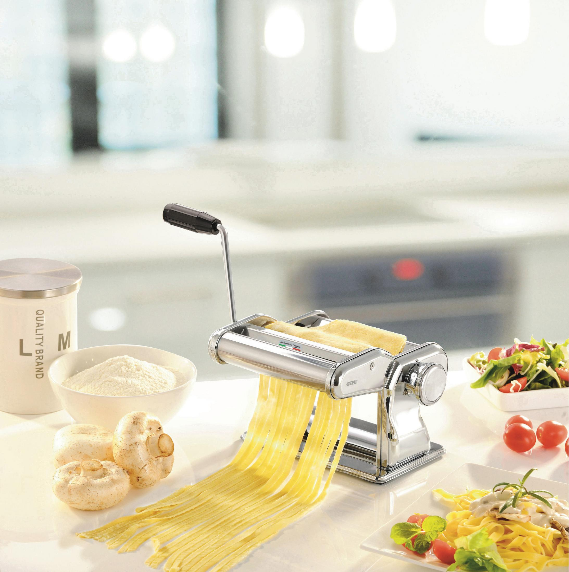 Nudelmaschine mit frischer Pasta, Mehl und Zutaten. Hintergrund: Küchentheke.
