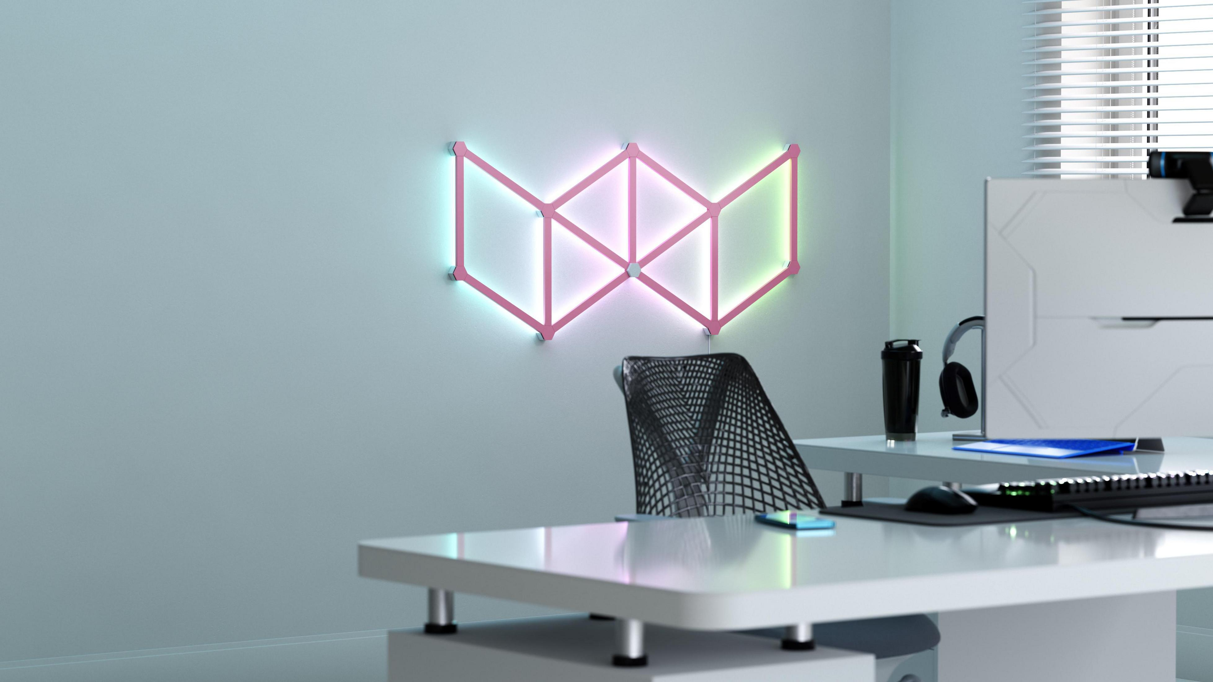 Eine an der Wand befestigte, rosa, geometrische Leuchte über einem Schreibtisch in einem Büro.
