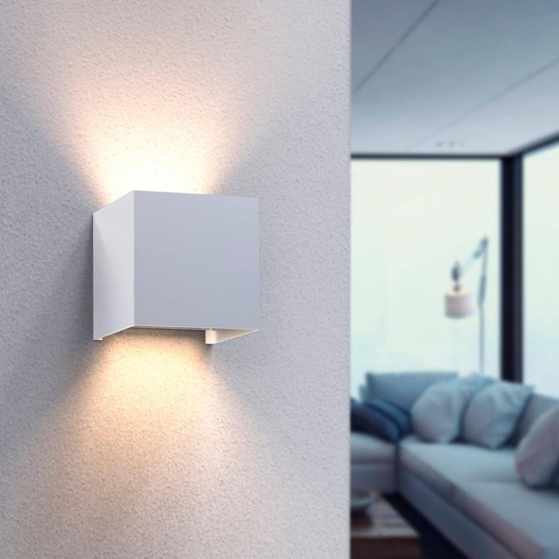Weiße quadratische Wandleuchte mit zwei Lichtstrahlen an einer weißen Wand, in einem Wohnzimmer.