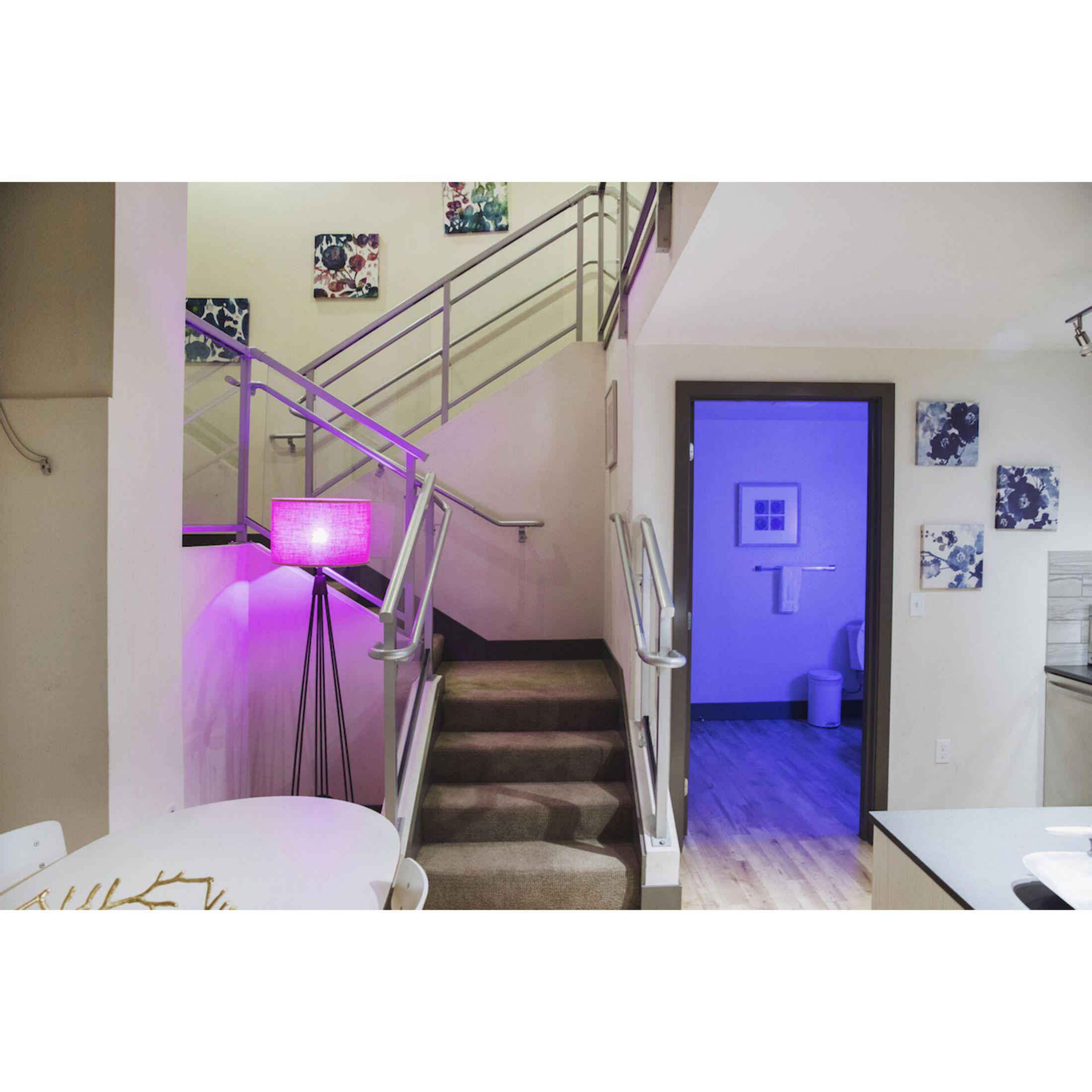 Treppe mit rosa Lampe, Kunst und Tür zu blau beleuchtetem Raum.