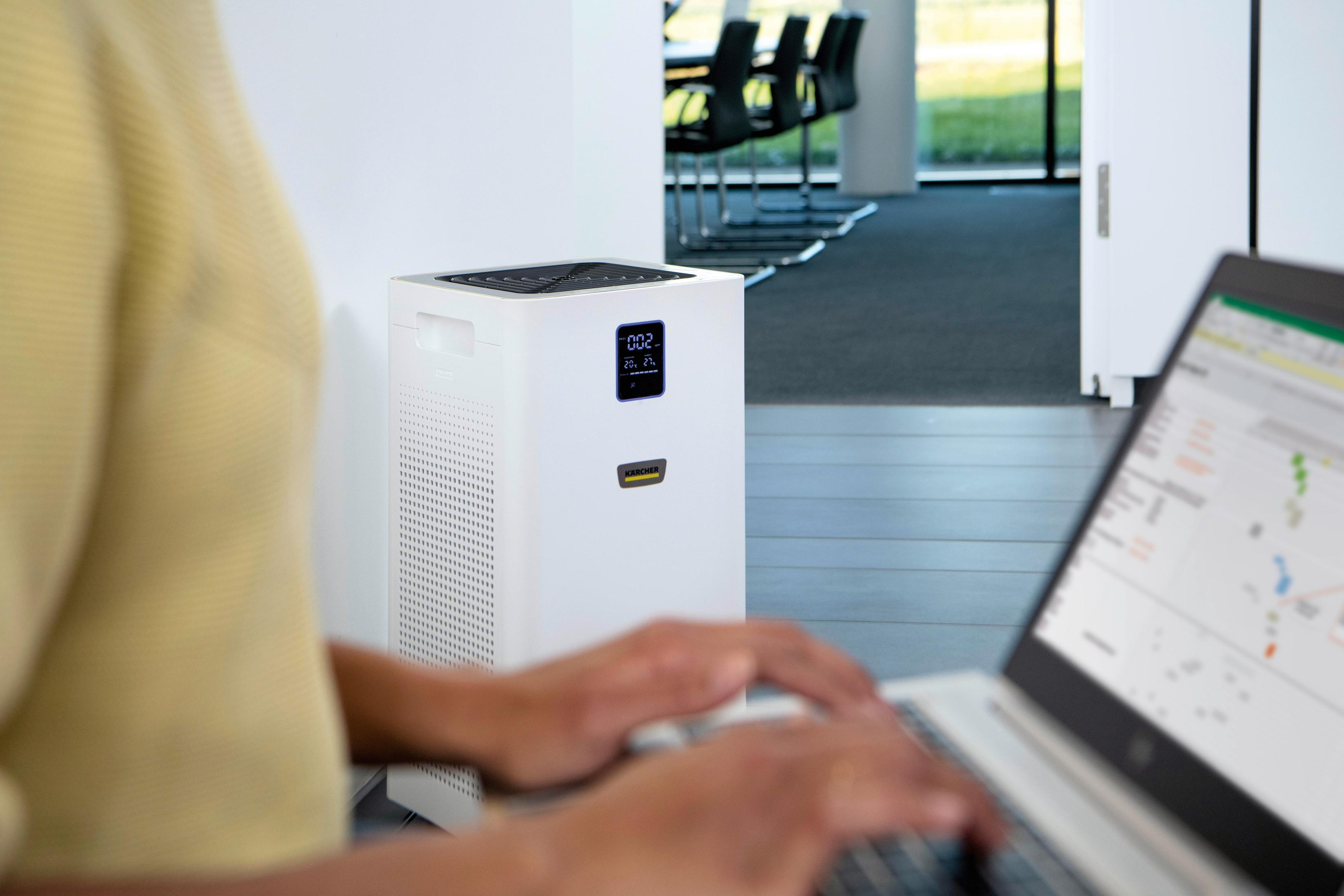 A person working on a laptop in an office next to a white air purifier.
