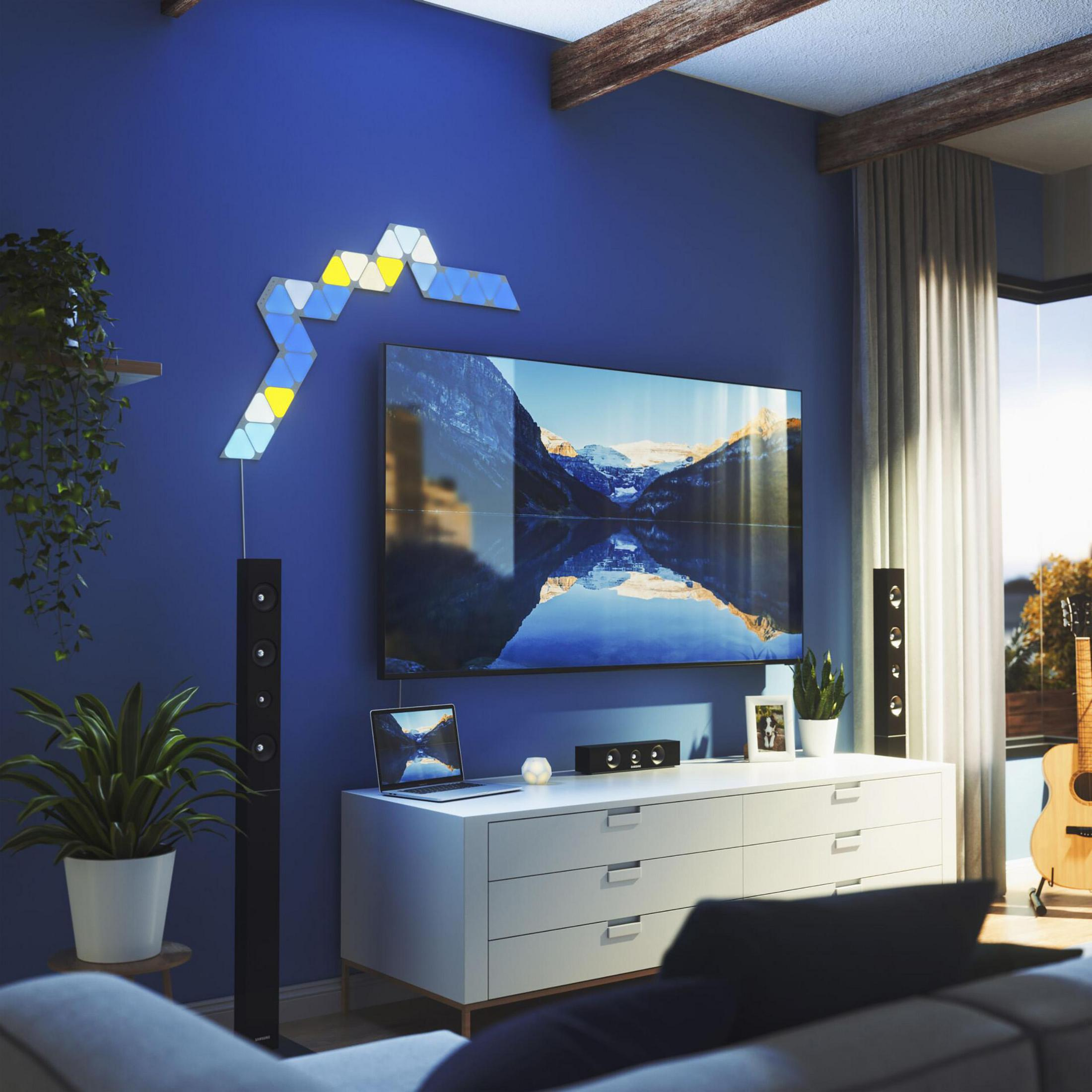 Una stanza con un muro blu, una TV e un pannello di luci triangolari. Una coppia è seduta sul divano.