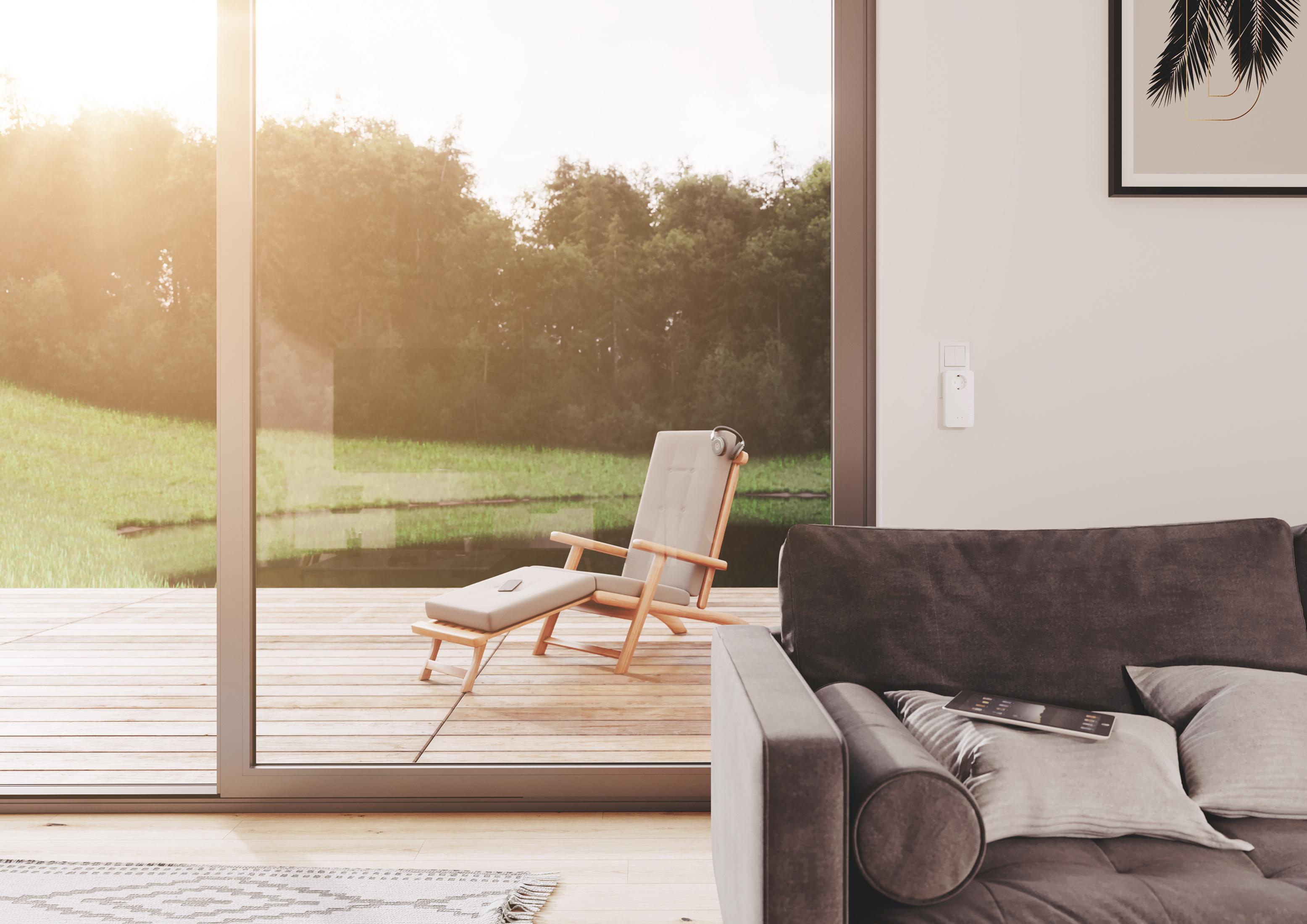 Ein sonnendurchflutetes Interieur mit Holzterrasse, Stuhl, Couch und Blick auf einen See.