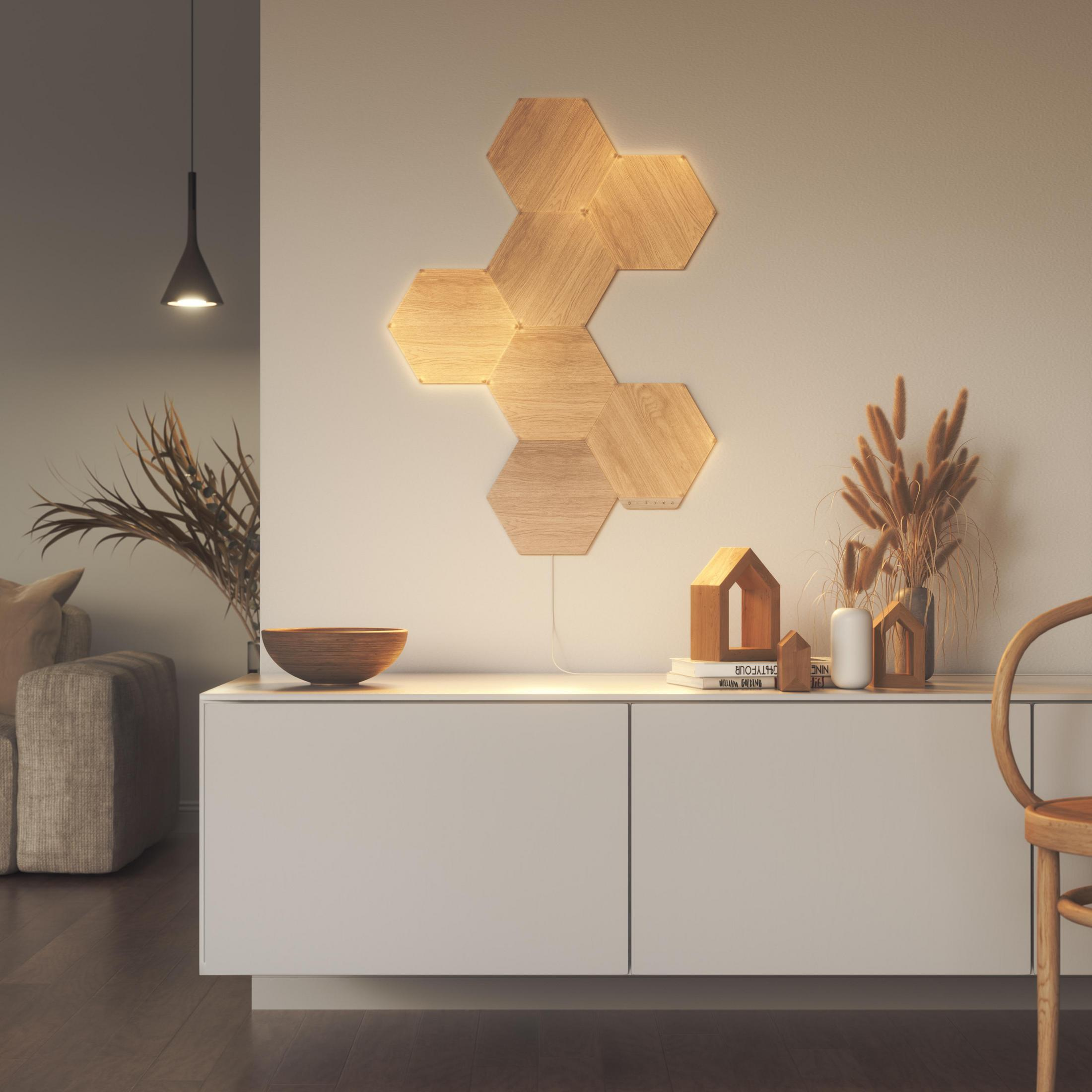 Lampade da parete esagonali in legno su un muro bianco, con decorazioni su un mobile bianco.