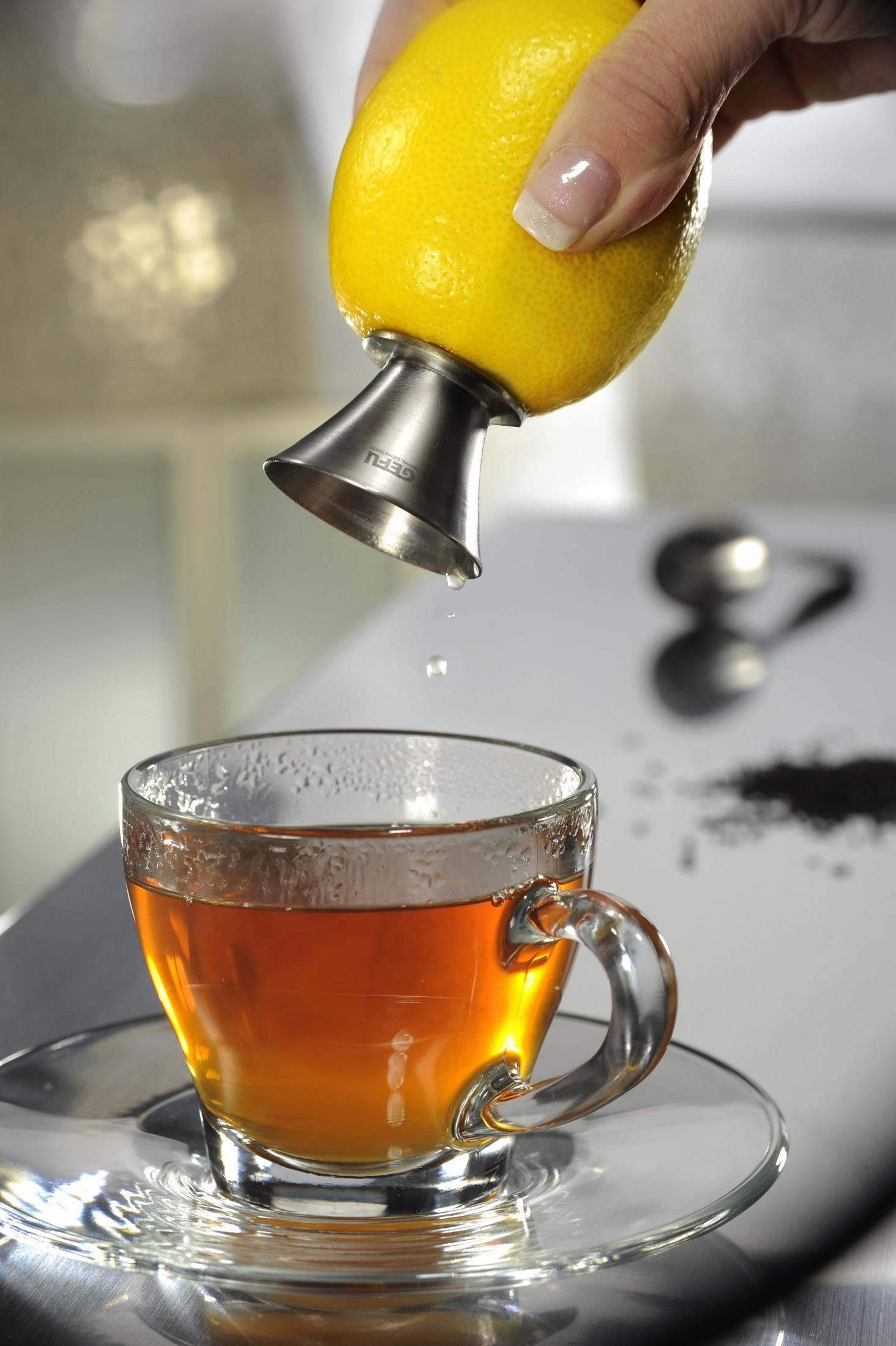 Hand presst Zitronensaft in ein Teeglas. Klares Glas mit Tee auf Untertasse.