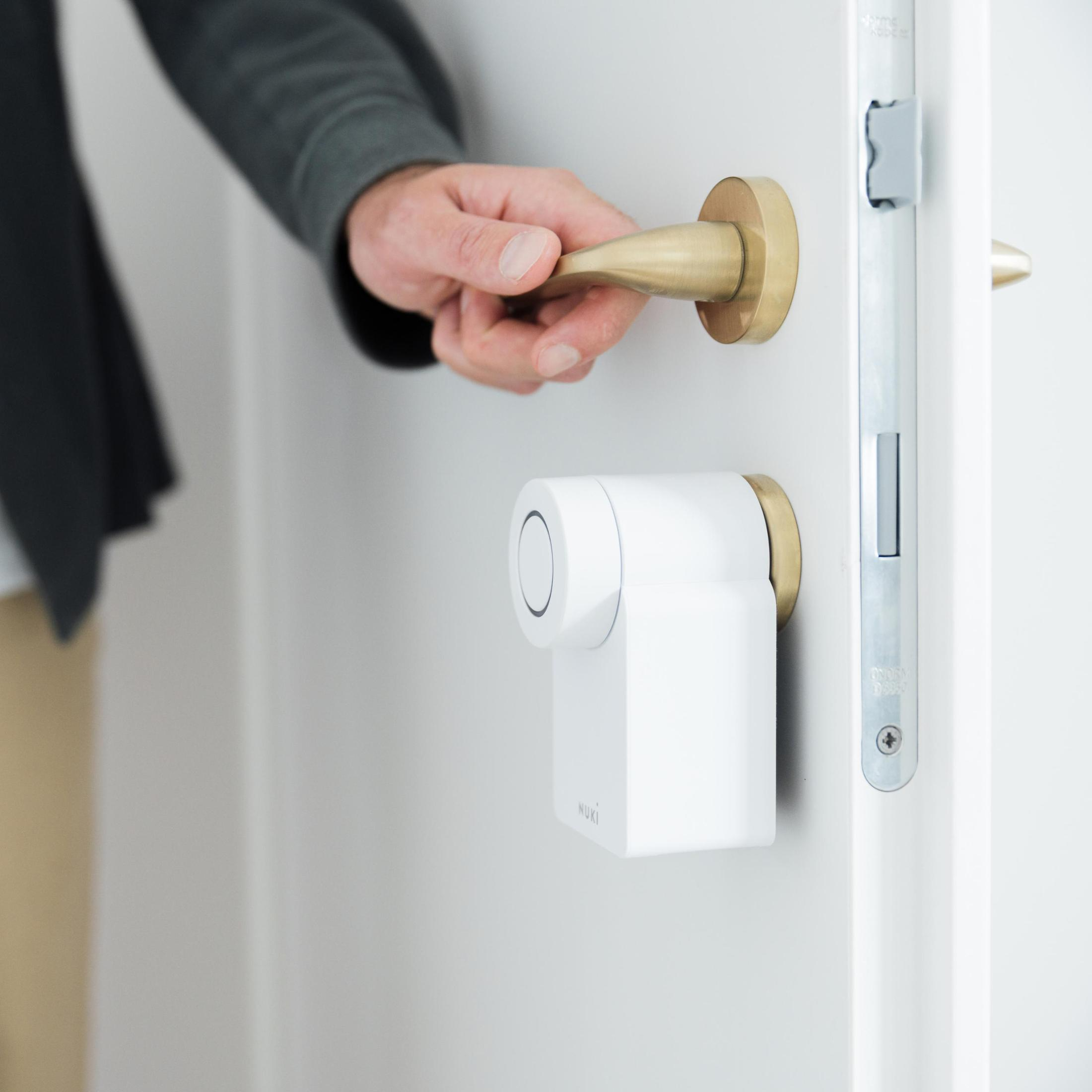 Eine Hand öffnet eine Tür mit einem installierten weißen Smart Lock.