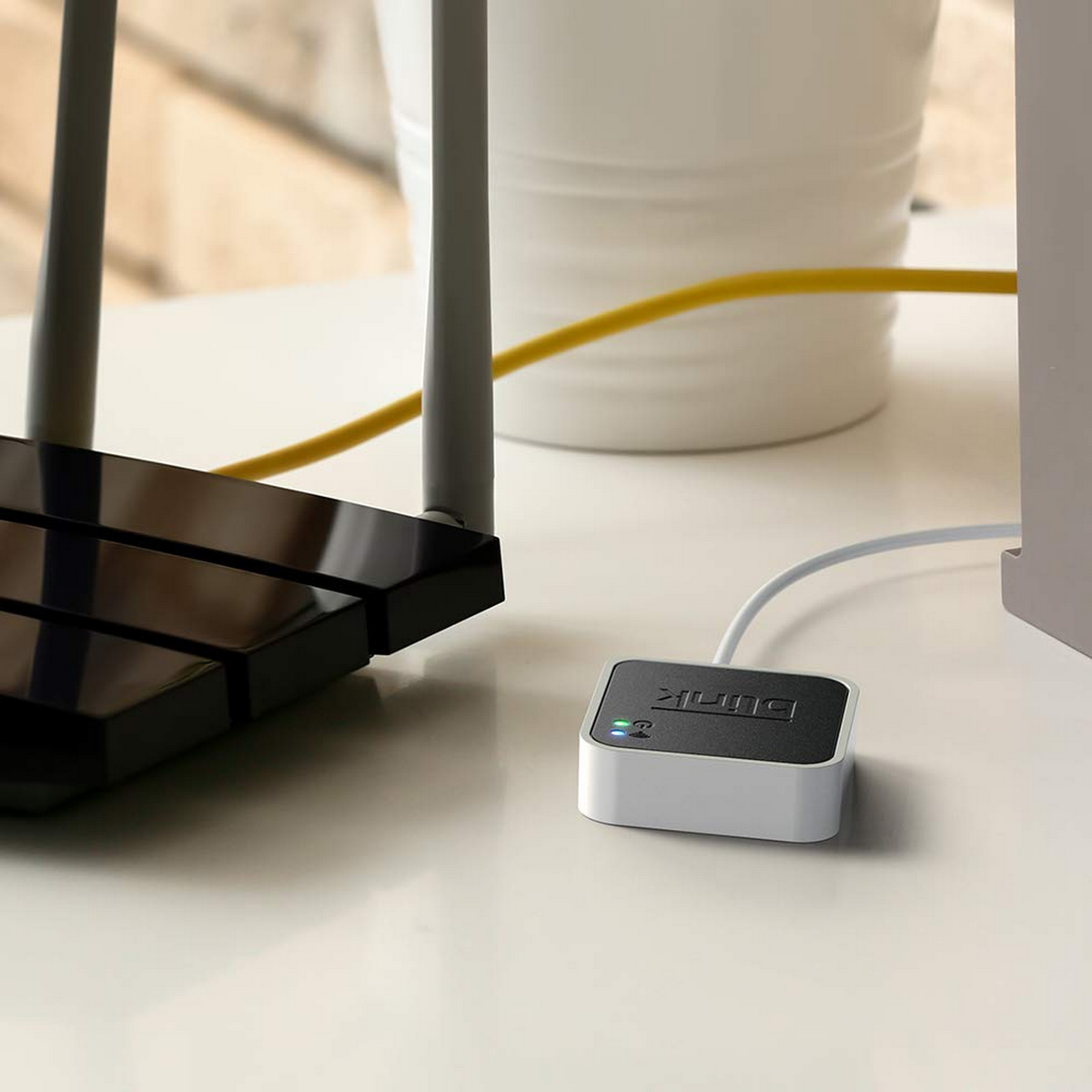 Ein weißer und schwarzer Router mit Antennen steht auf einem weißen Tisch und ist mit einem kleinen schwarzen Gerät verbunden.