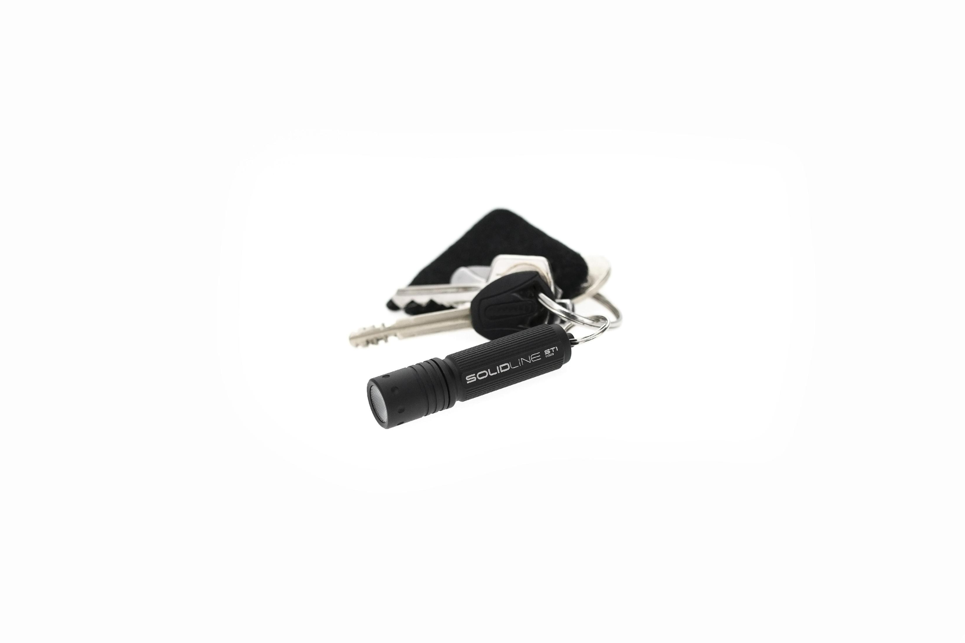 Eine schwarze Taschenlampe mit Schlüsselring und Schlüsseln. Auf weißem Hintergrund.