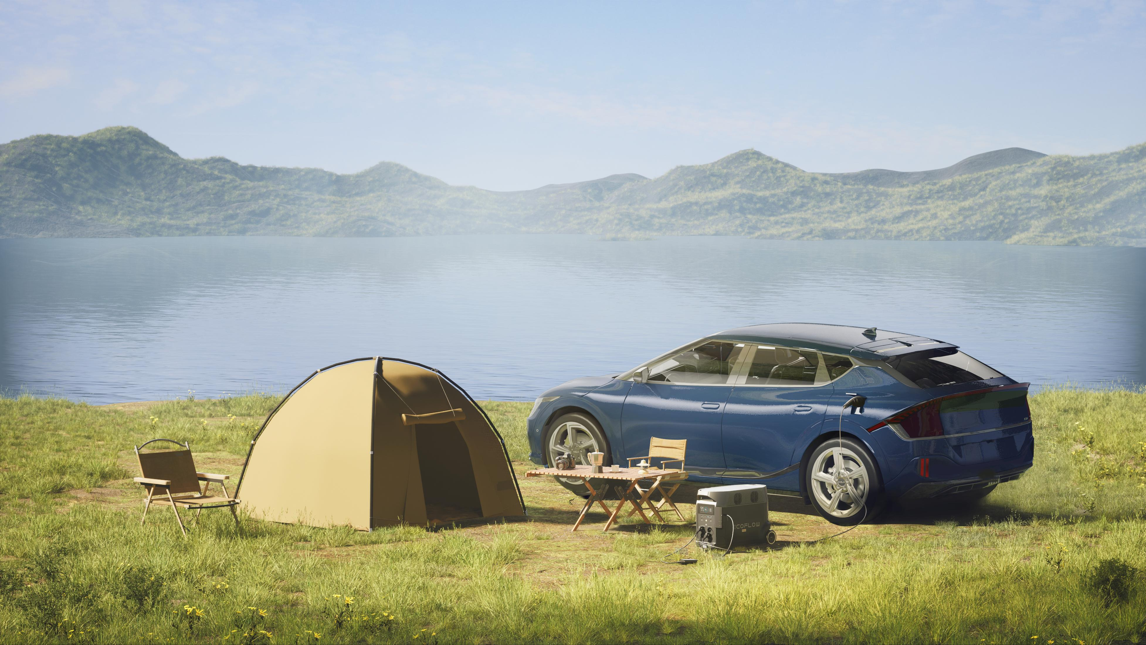 Auto blu vicino a tenda, tavolo e sedie vicino a un lago con montagne sullo sfondo.