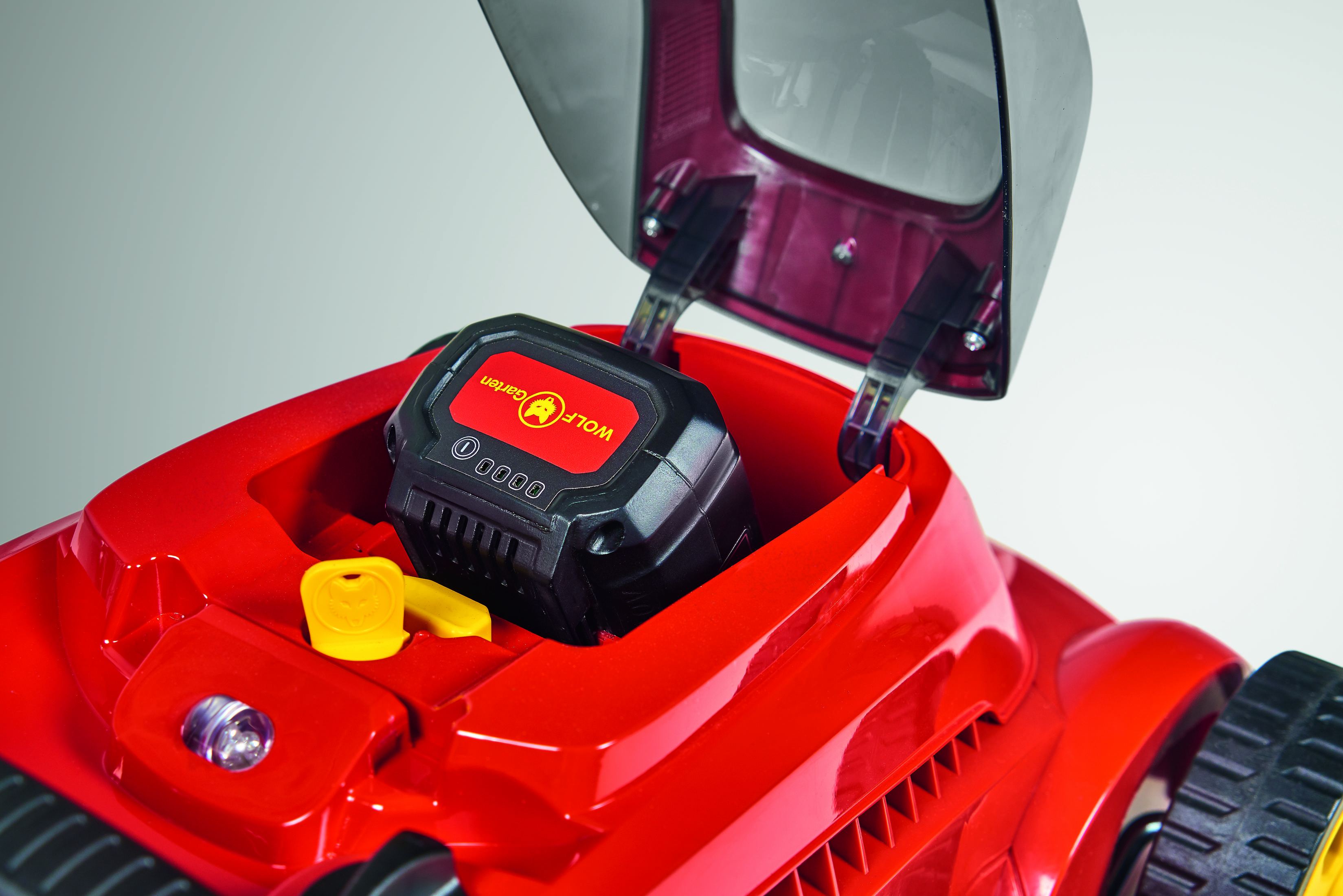 Roter Rasenmäher mit offenem Deckel. Batterie ist innen. Gelber Schlüssel und schwarze Batterie.