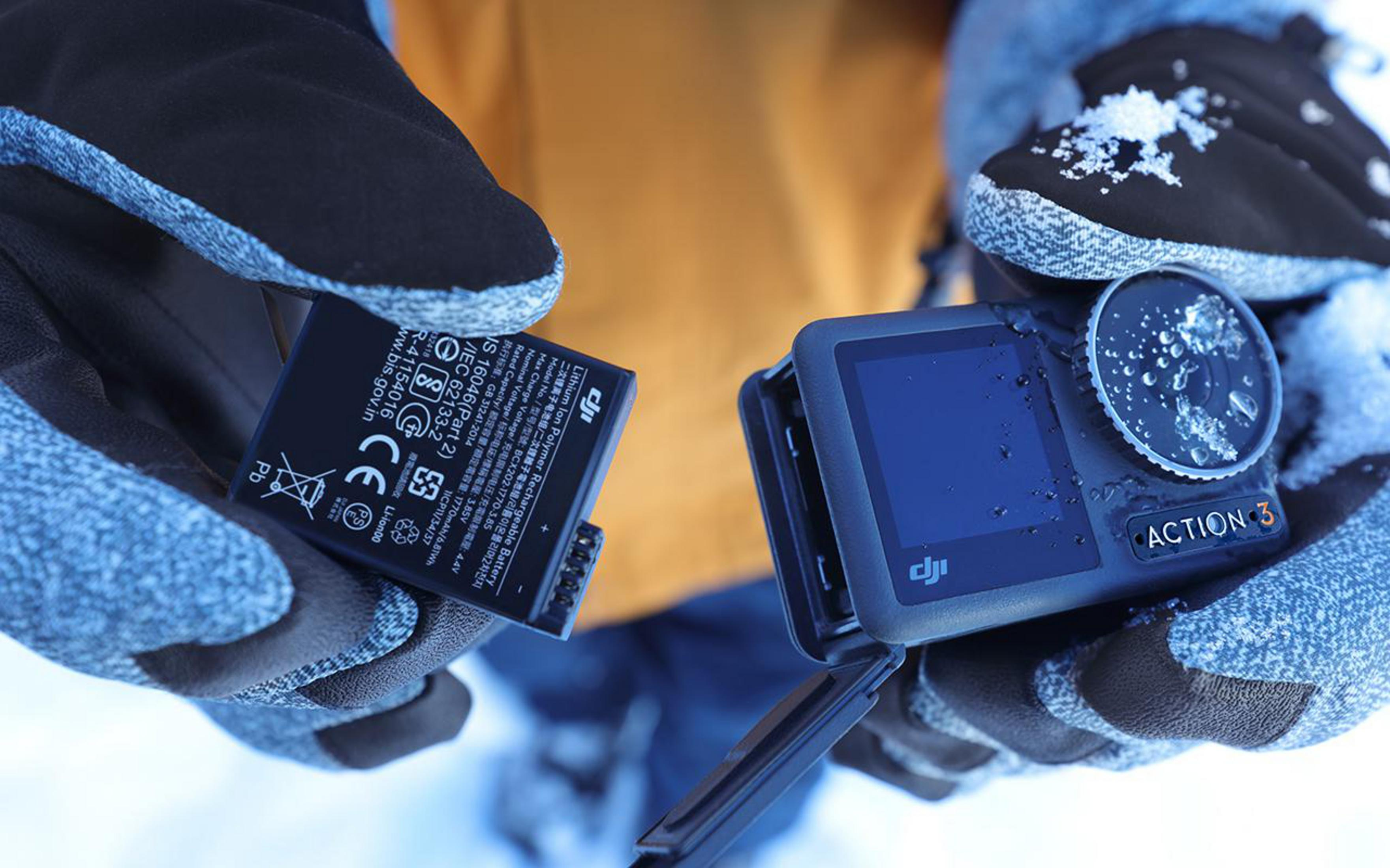 Ręce trzymające baterię i aparat, oba czarne.