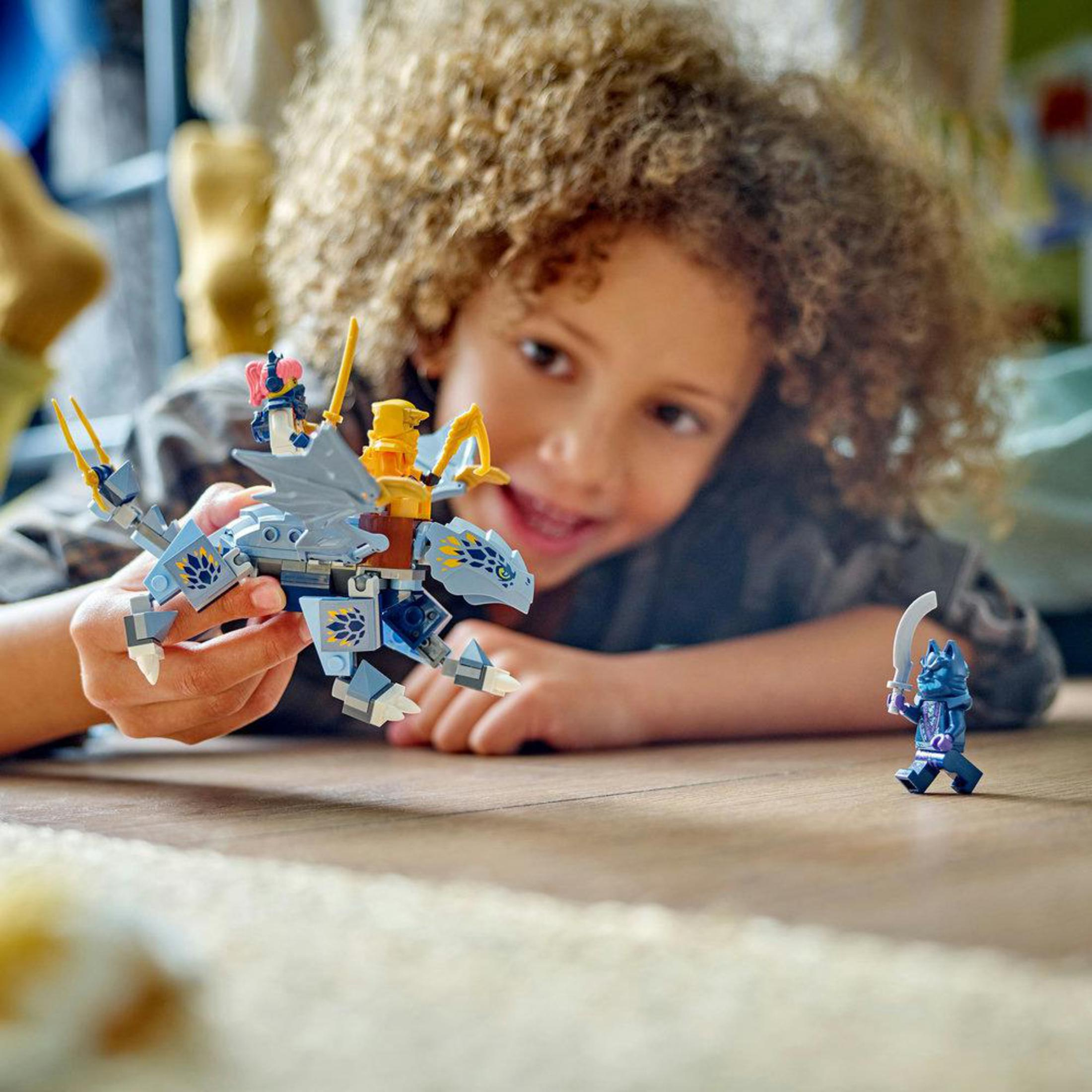 Kind spielt mit Lego. Ein Drache und eine Minifigur befinden sich auf einem Holzboden.