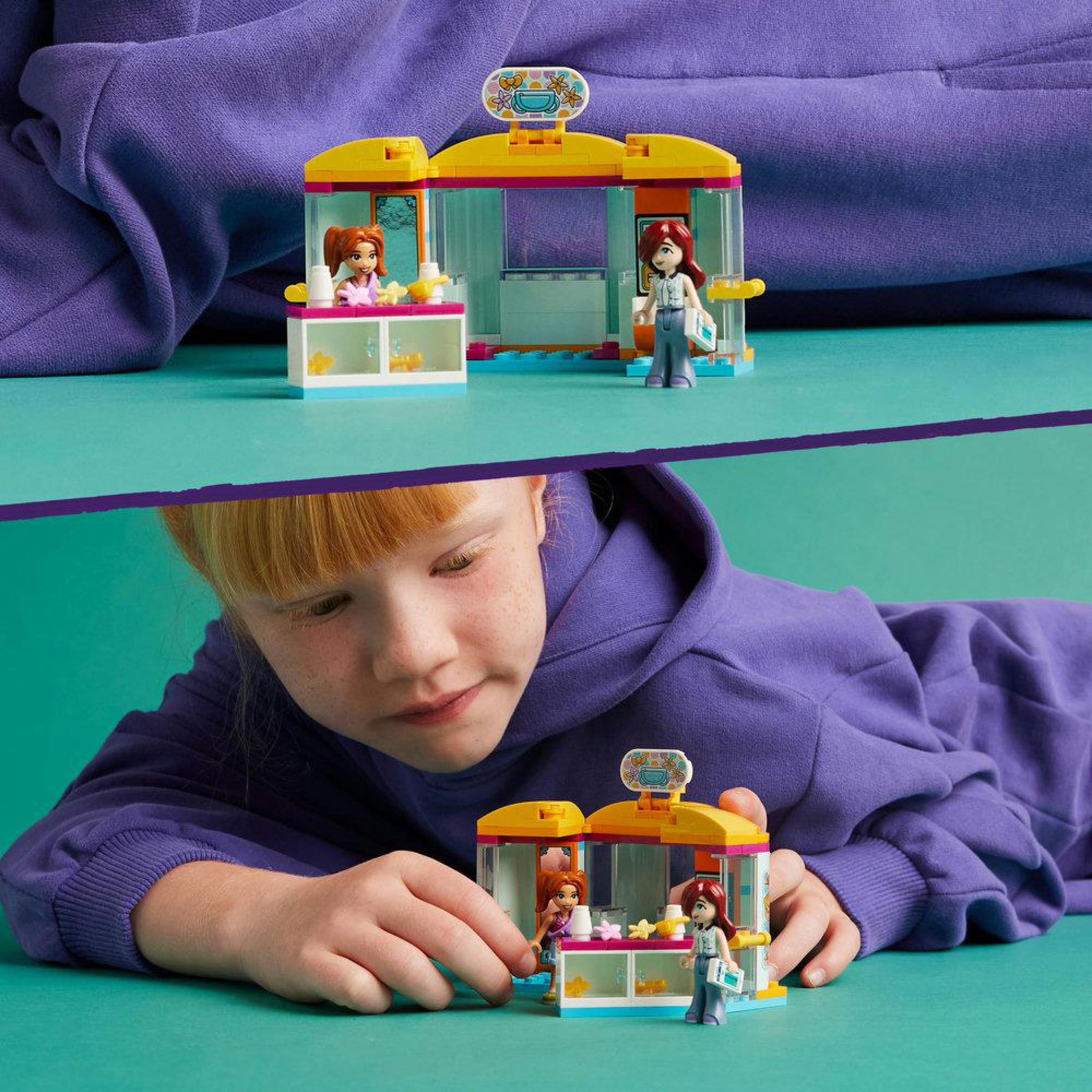 Kind interagiert mit Lego Friends Set. Set zeigt Shop mit Figuren, Mädchen im Vordergrund.