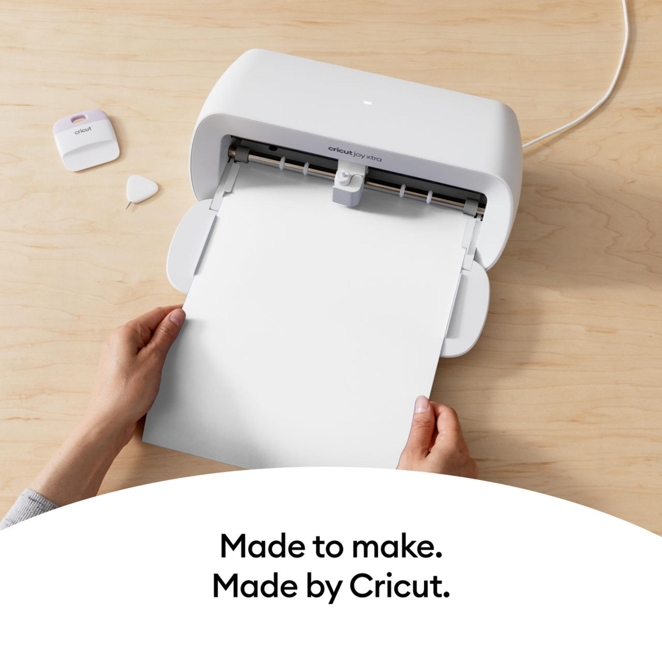 Weiße Cricut-Maschine, in die ein weißes Blatt Papier eingeführt wird. Hände sichtbar.