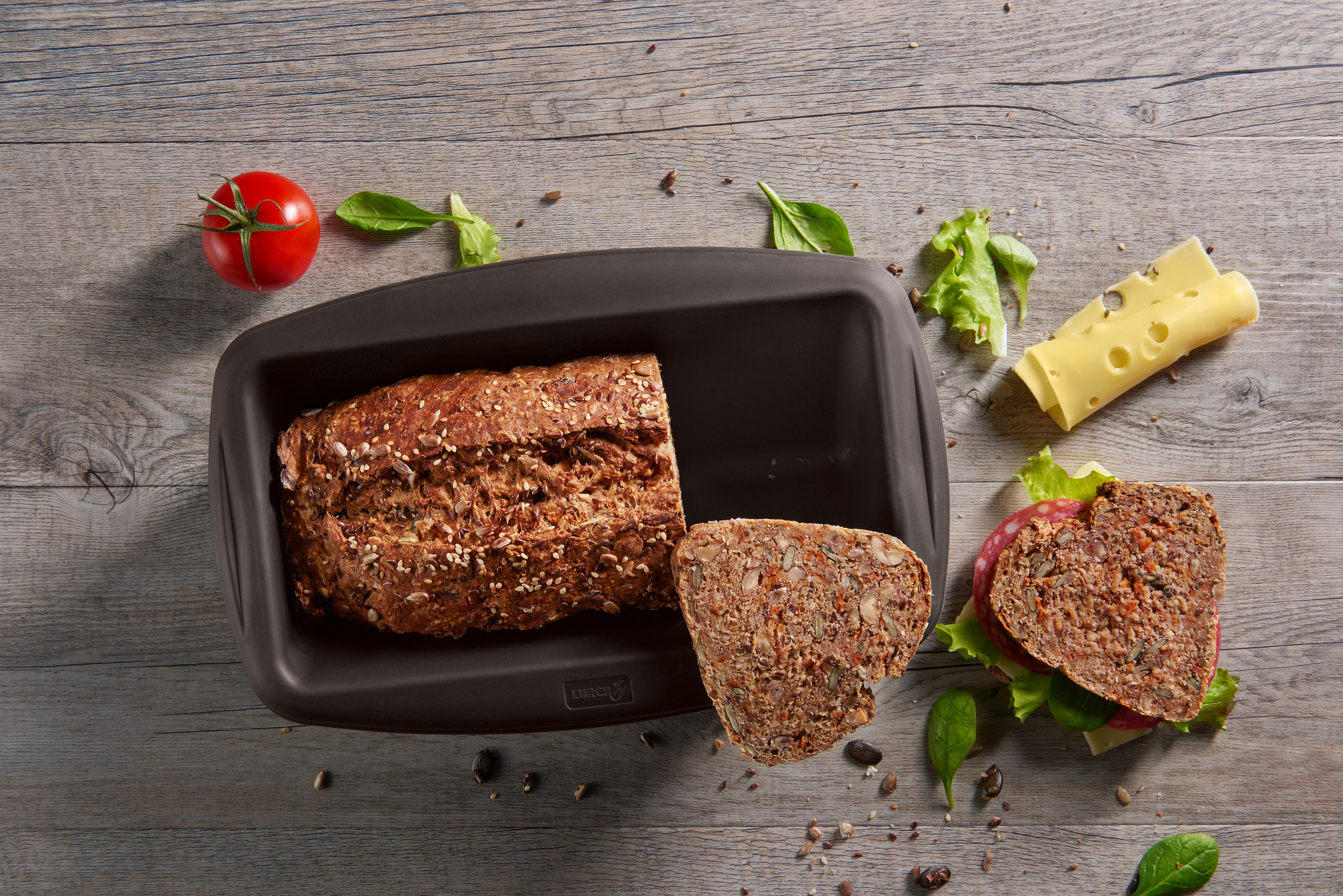 Ein Brotlaib in einer Backform, mit Tomate, Käse und Salat.
