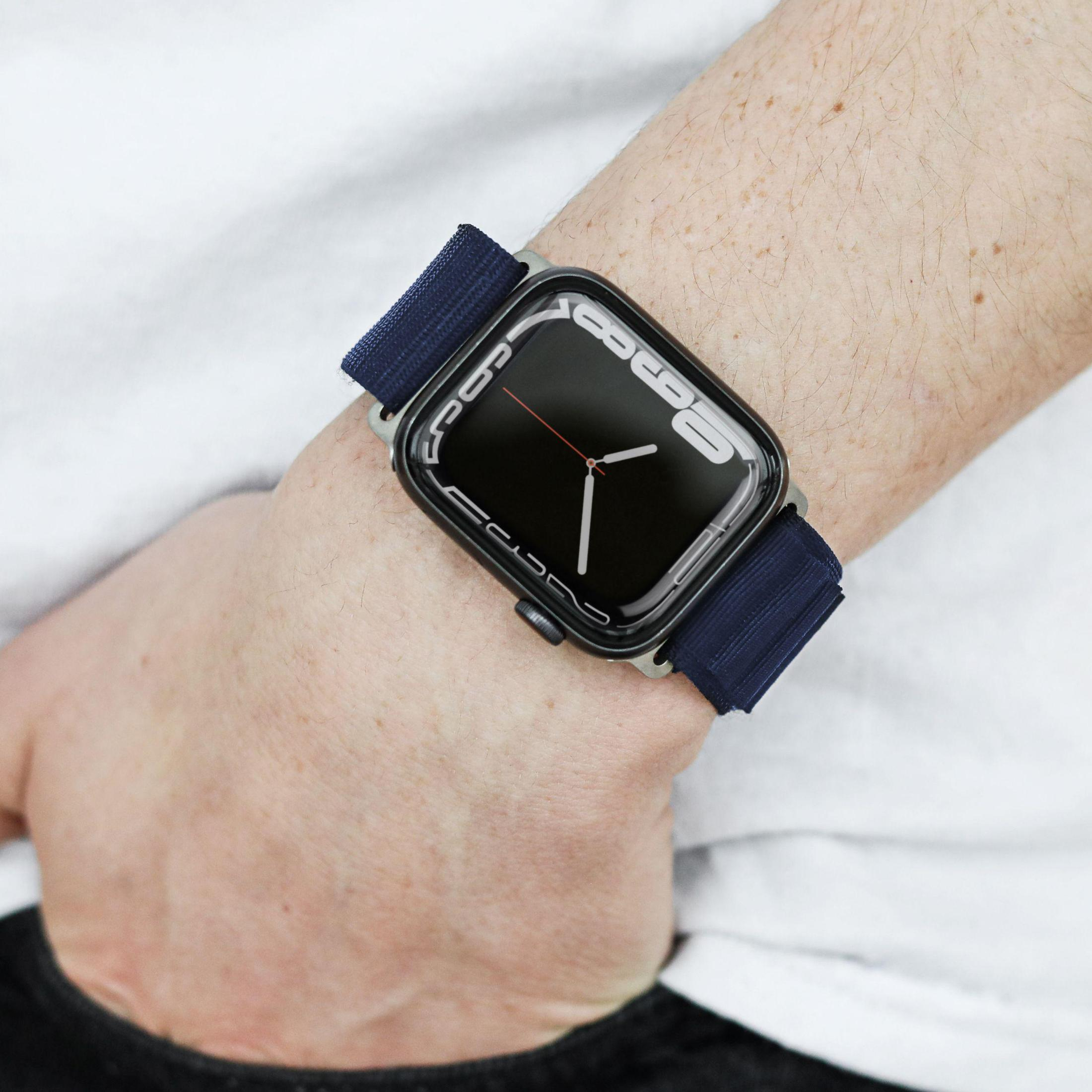 Handgelenk mit Apple Watch. Die Uhr hat einen dunklen Bildschirm und ein marineblaues Armband. Der Hintergrund ist weiß.