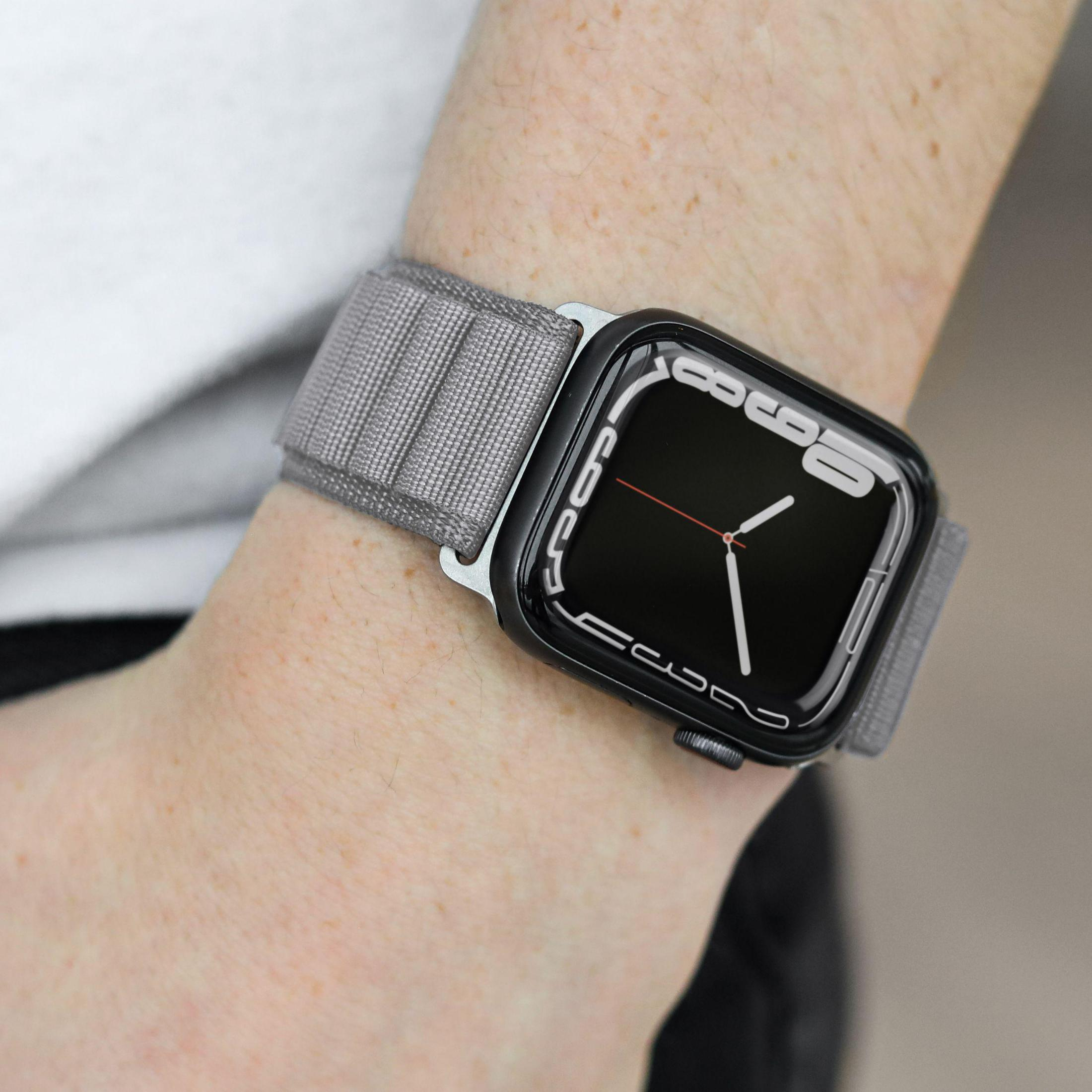 Osoba nosząca smartwatch z szarym materiałowym paskiem. Tarcza jest czarna.