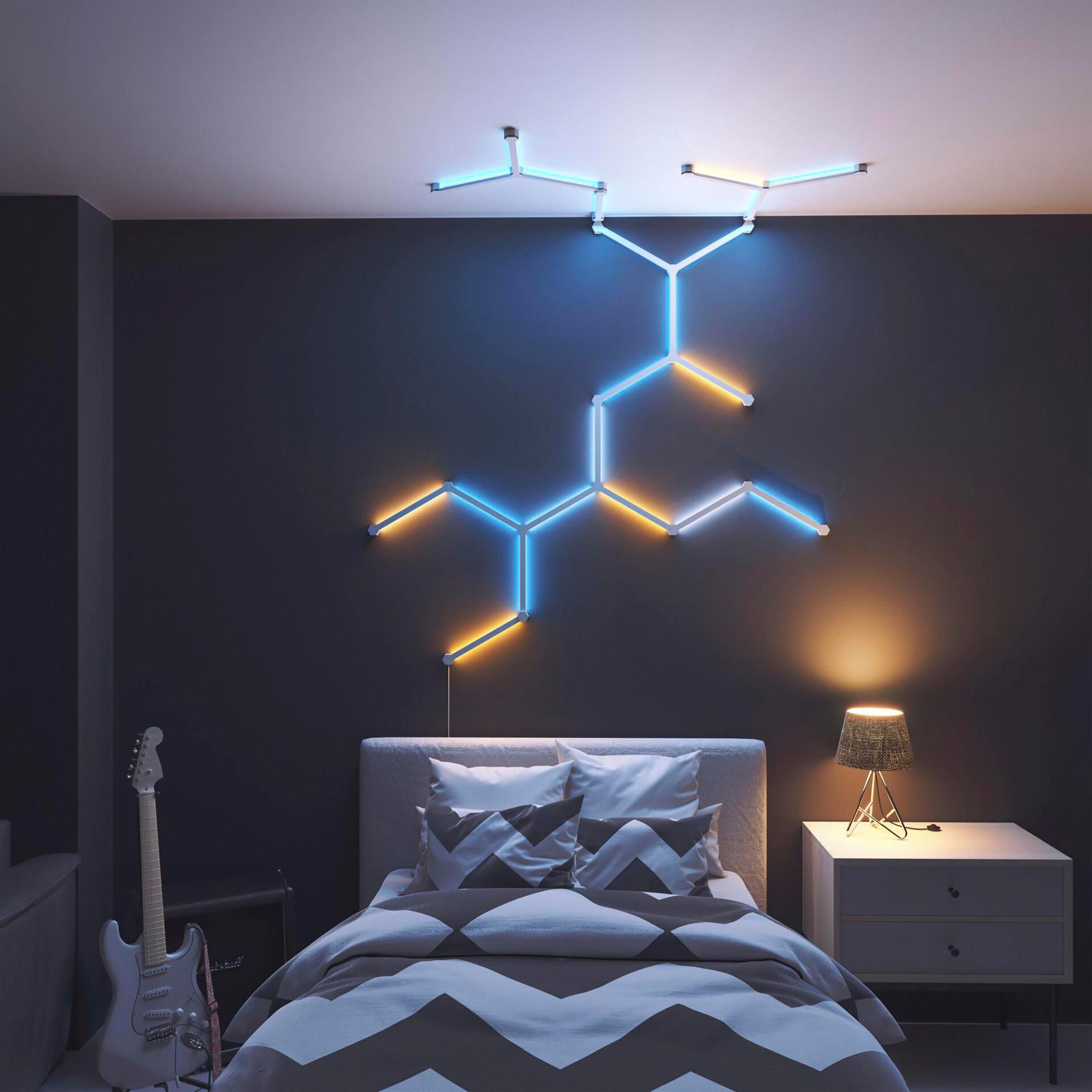 Ein Schlafzimmer mit Neonlichtern an der Wand. Ein Bett mit Kissen und eine Gitarre sind sichtbar. Es hat eine dunkelgraue Wand.