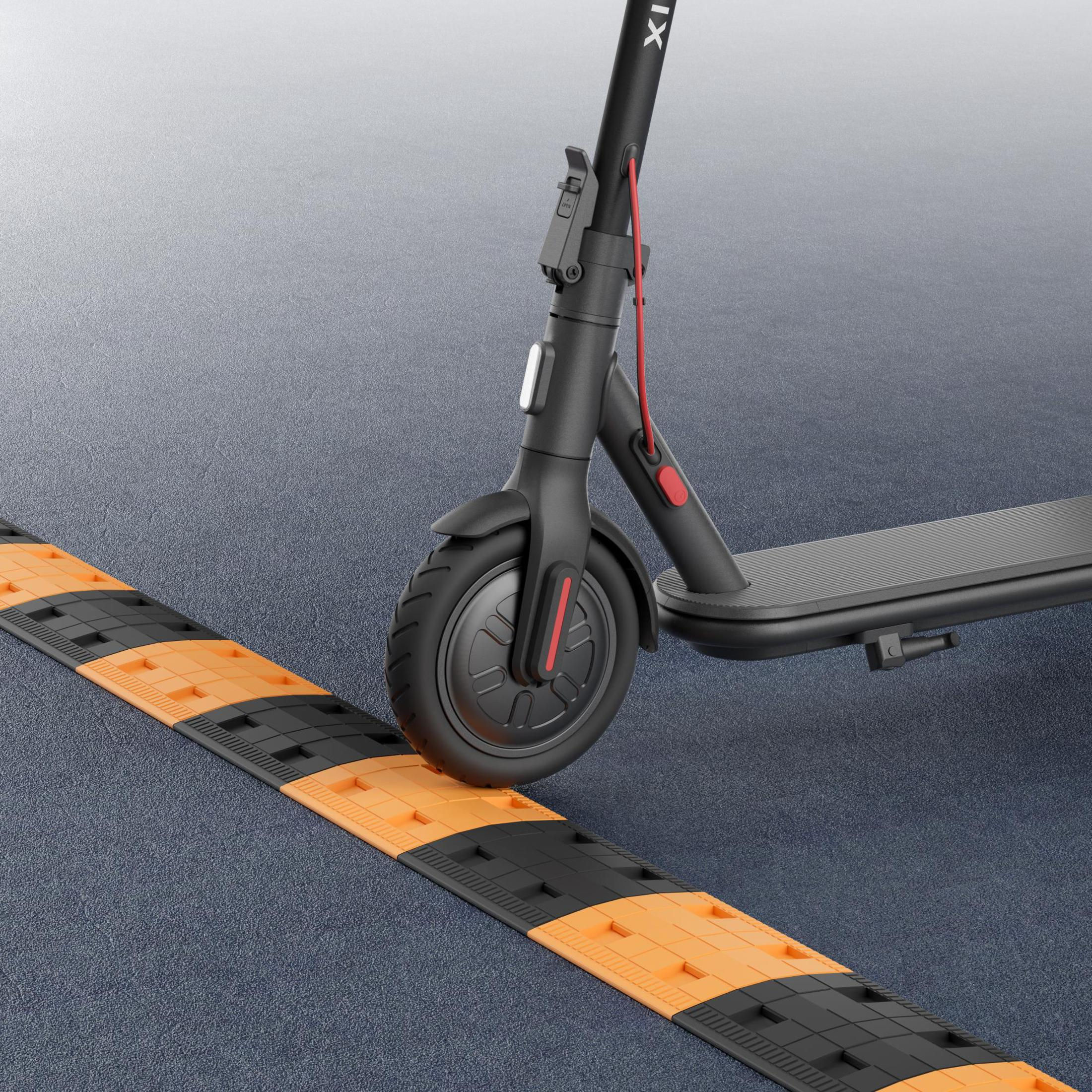 Schwarzer Elektroroller nähert sich einer Bodenwelle. Der Buckel ist orange und schwarz. Der Roller steht auf einer grauen Straße.