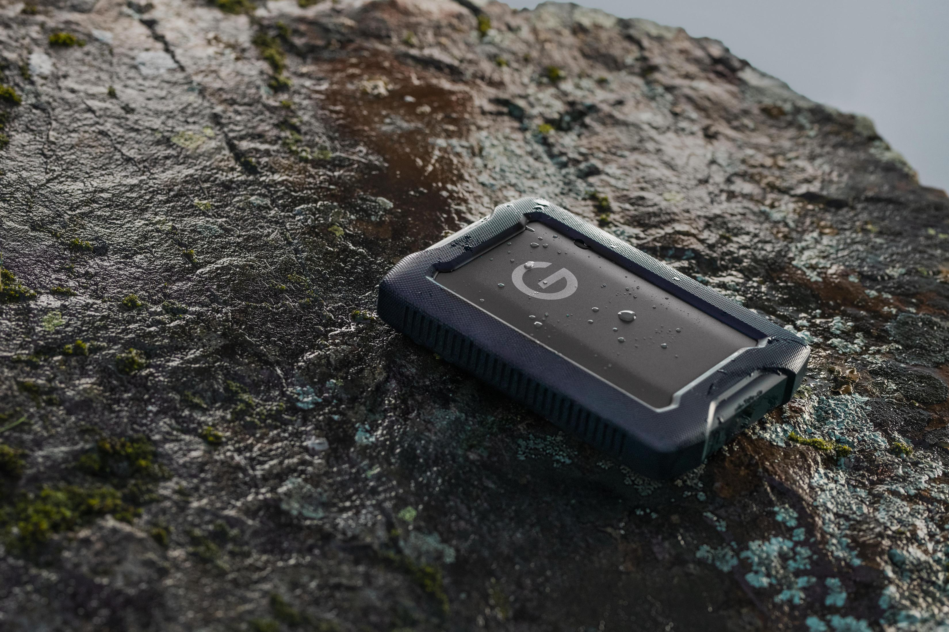 Czarny i niebieski zewnętrzny dysk twardy spoczywa na mokrej skale, z kroplami wody.