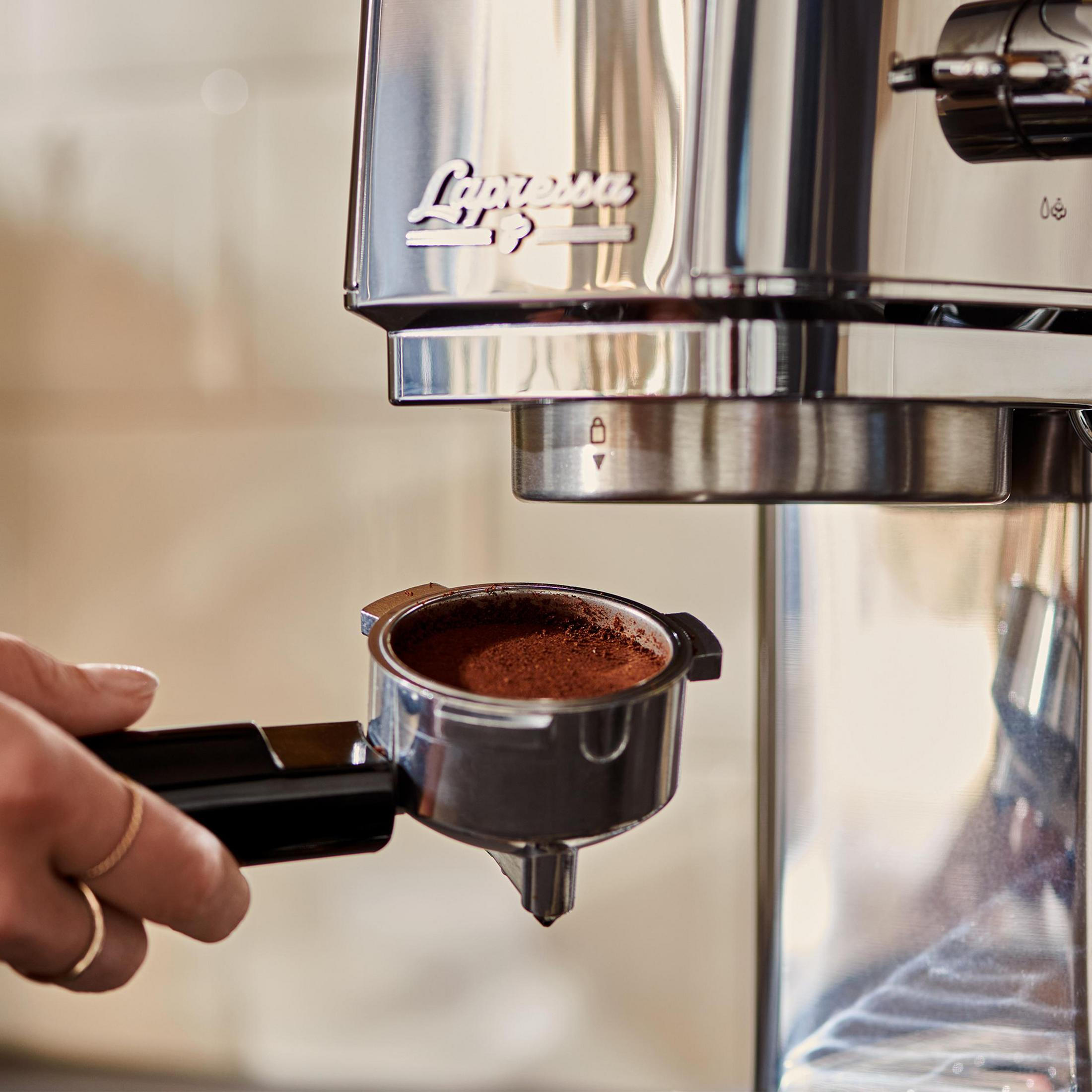 Una mano tiene un portafiltro pieno di caffè macinato sotto una macchina per espresso.