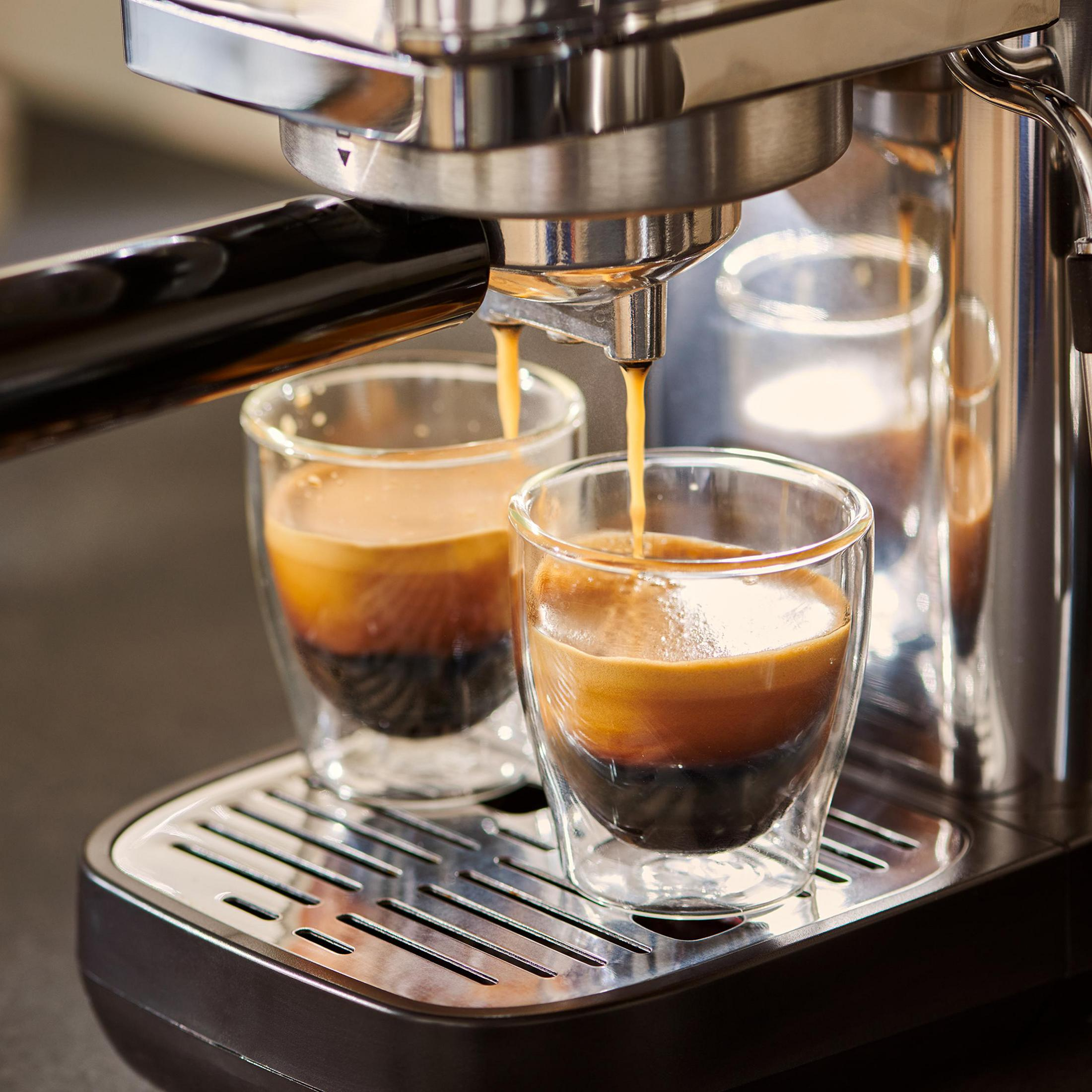 L'espresso cola in due bicchieri trasparenti da una macchina argentata su una vaschetta raccogligocce.