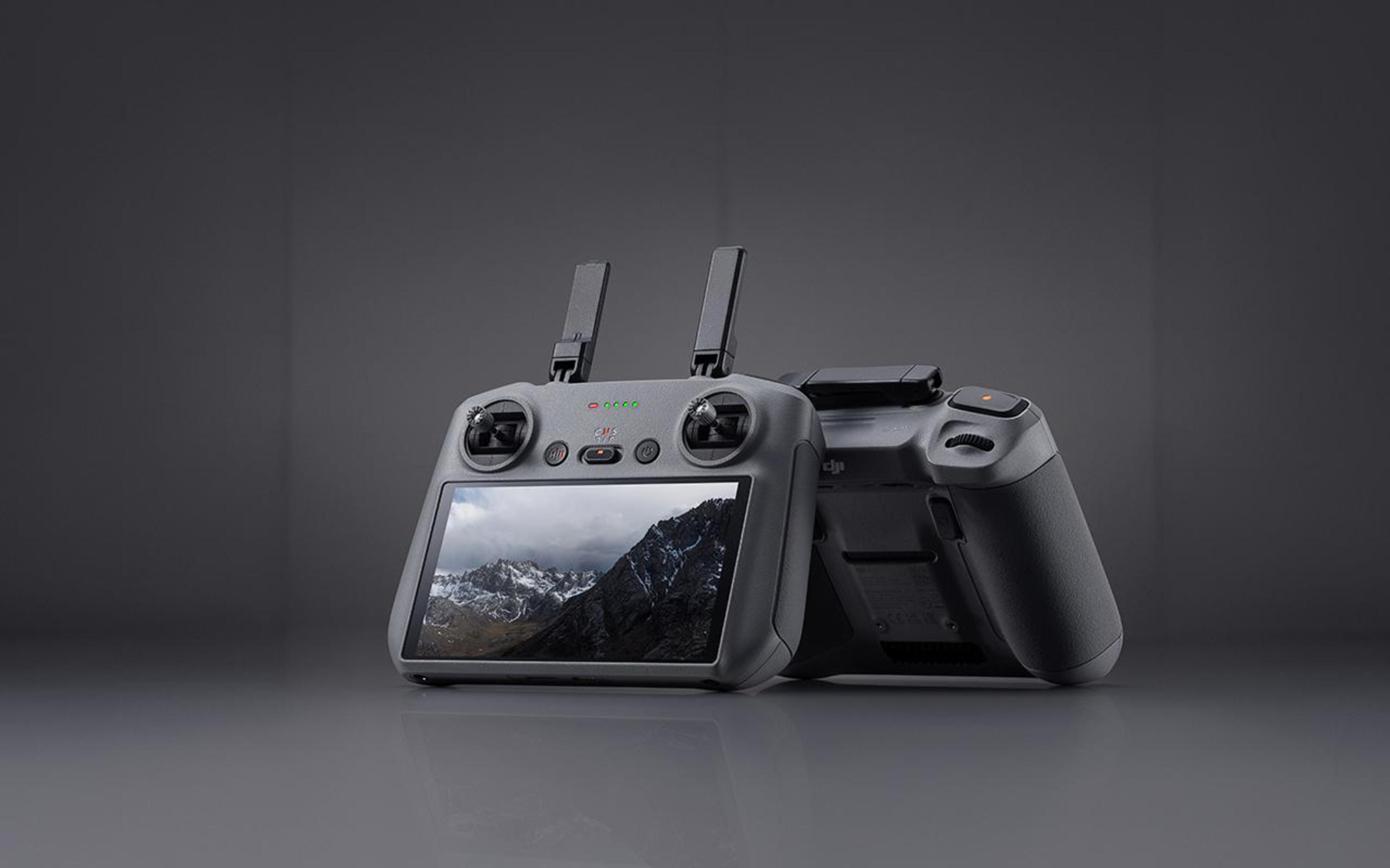 Zwei graue DJI-Drohnen-Controller mit Antennen. Einer zeigt einen Bildschirm mit Bergansicht.