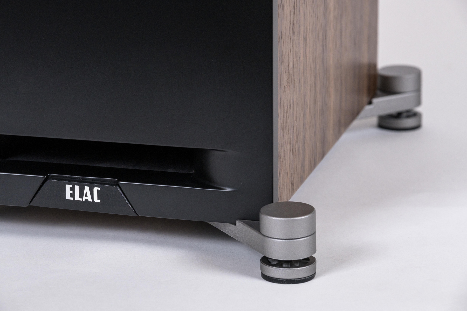 Nahaufnahme des Lautsprecherfußes. ELAC-Logo sichtbar. Braunes Holz und schwarze Details.