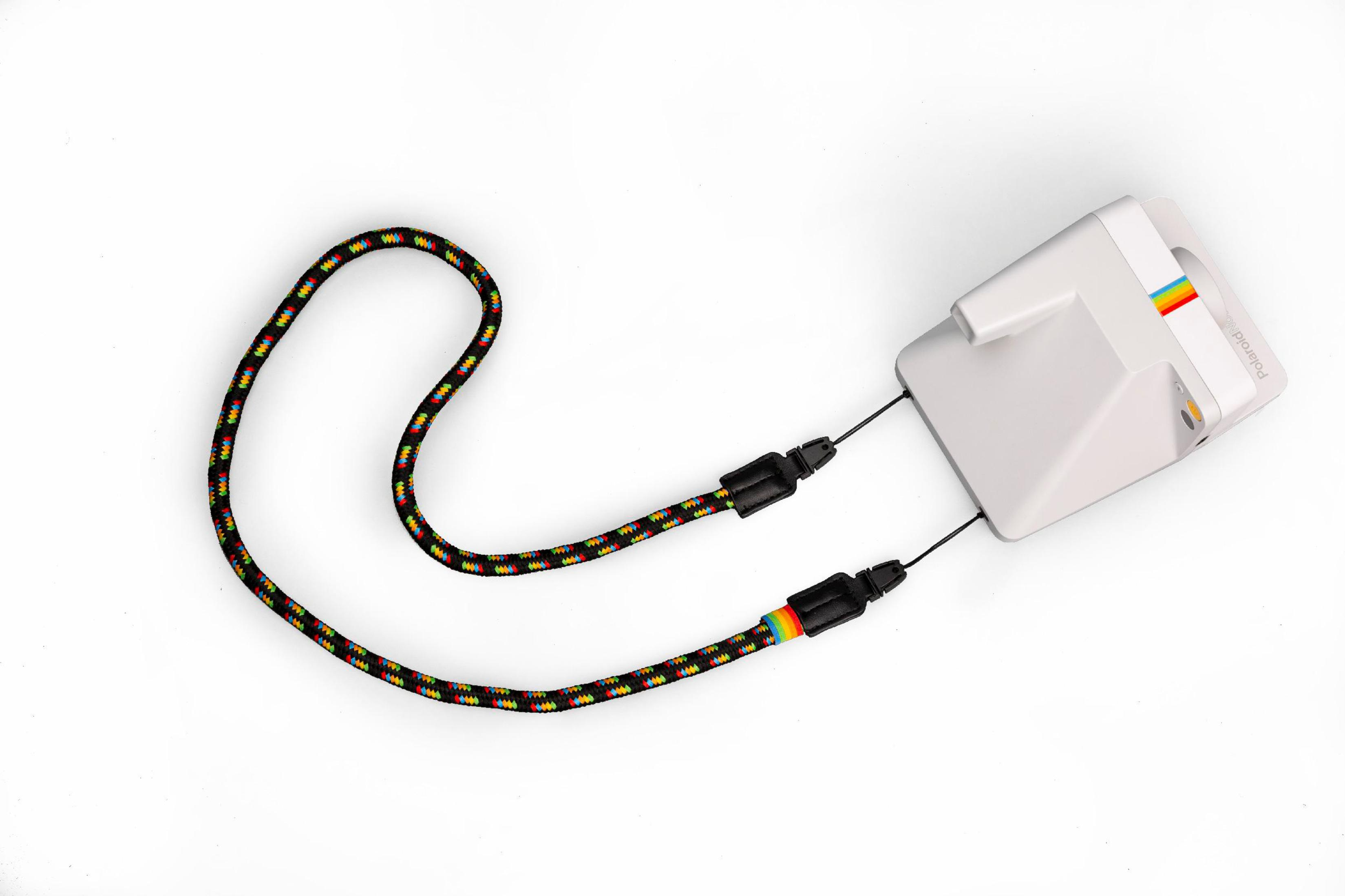 Biały aparat Polaroid z tęczową smyczą, na białym tle.