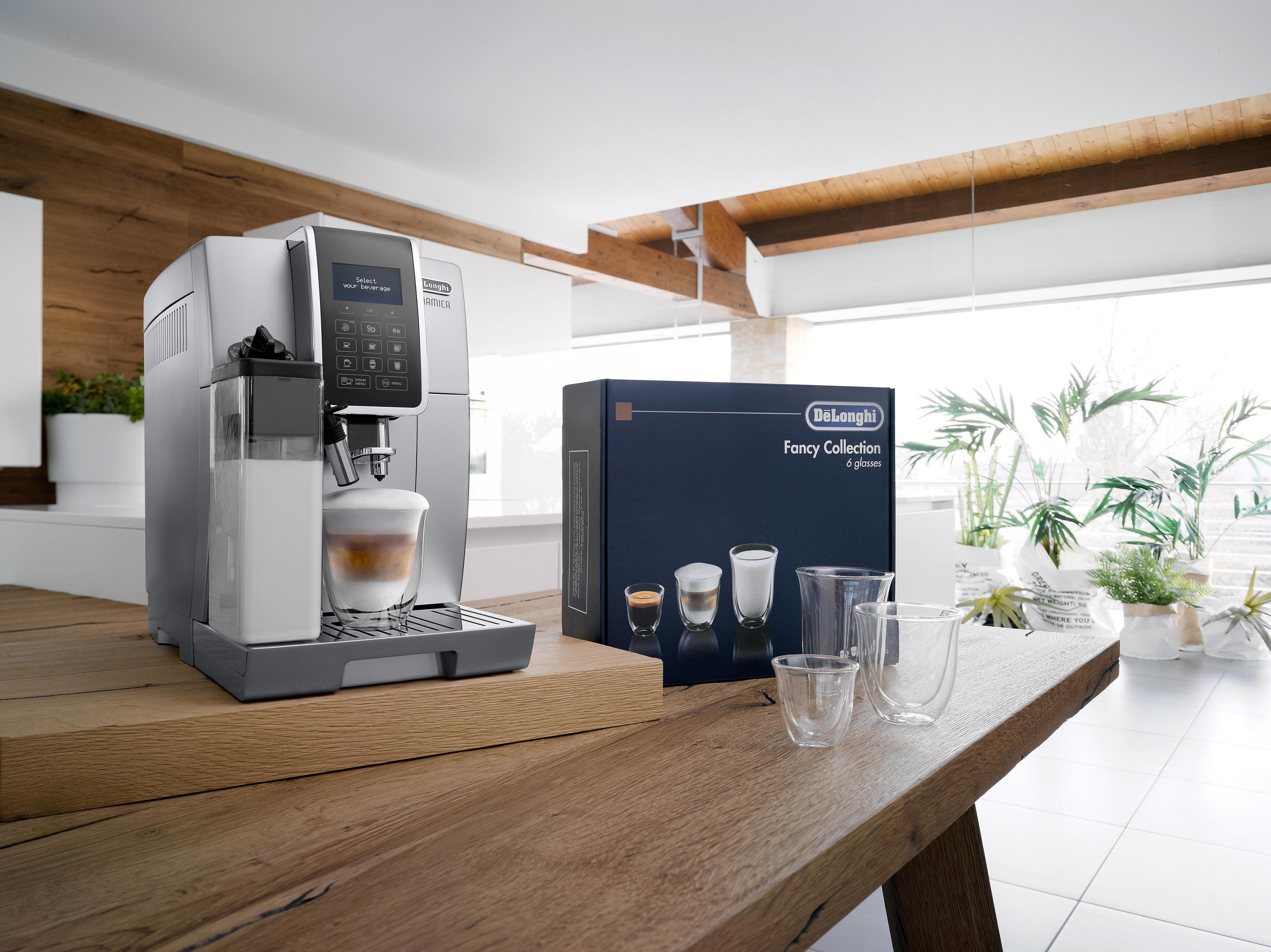 Silberne Kaffeemaschine. Kaffeegläser und eine Box auf Holztisch. Weißer Raum.