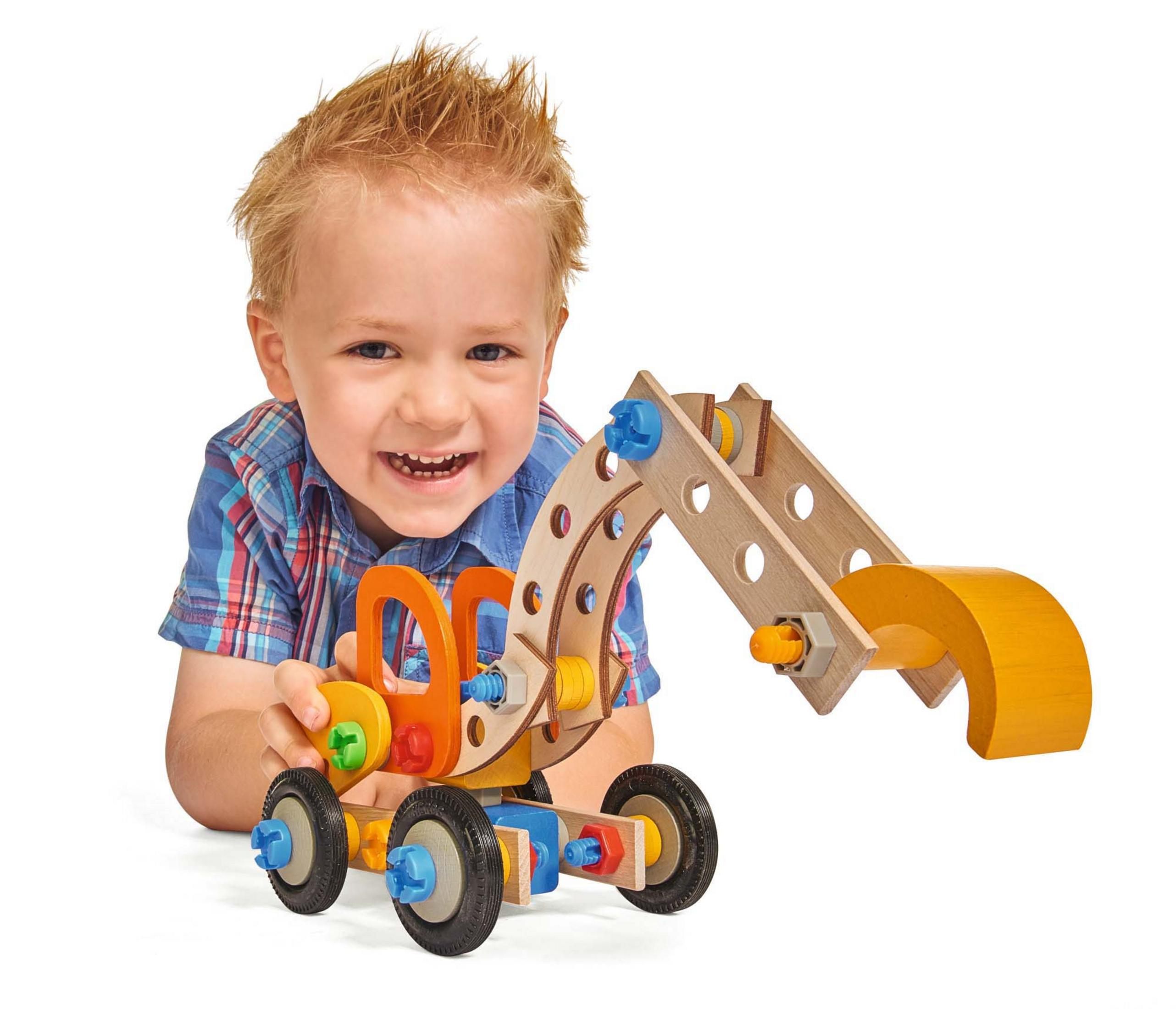 Chłopiec bawiący się drewnianą zabawką-koparką. Uśmiechnięty. Białe tło.