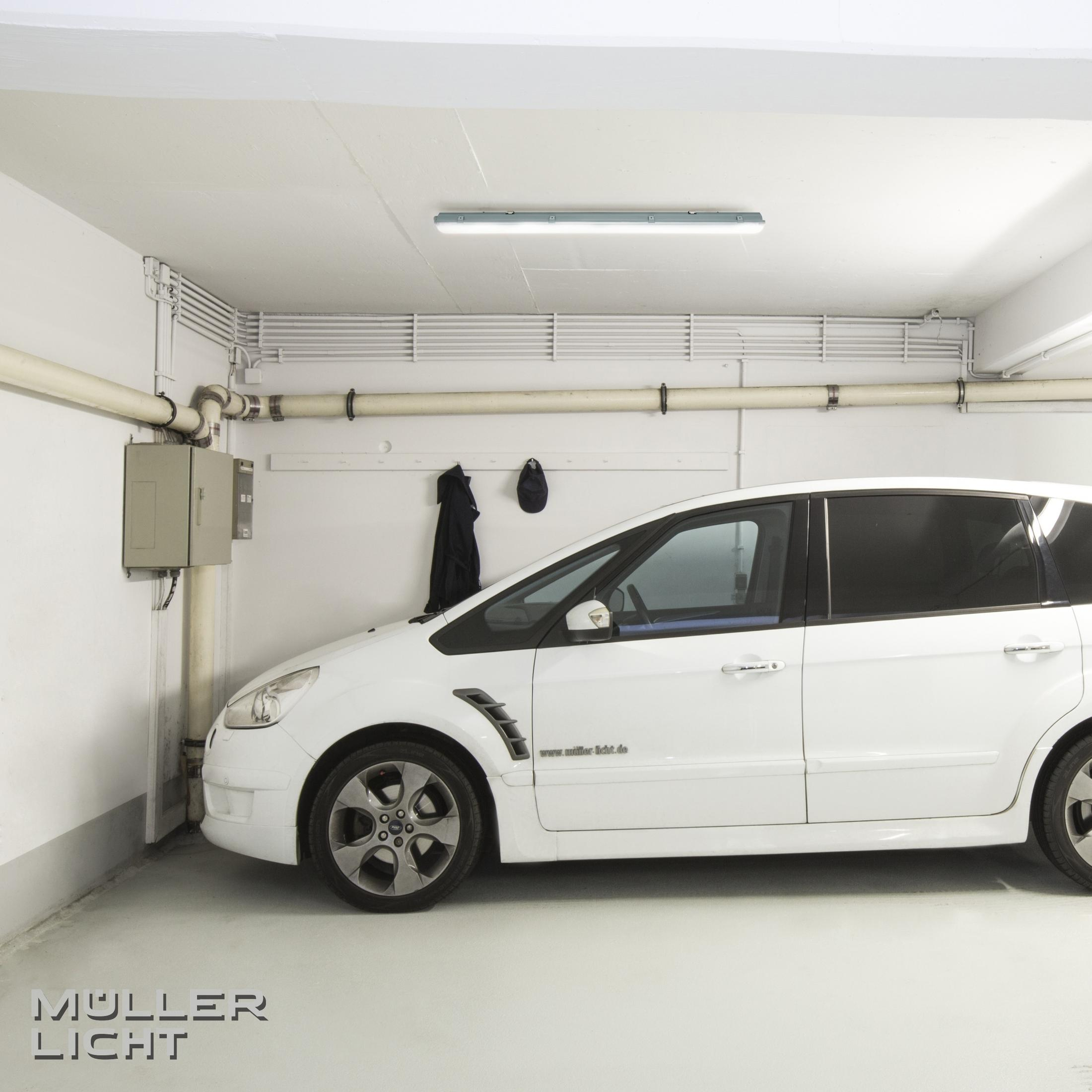 Un'auto bianca è parcheggiata in un garage con un'illuminazione sul soffitto. Ci sono tubi sul muro.