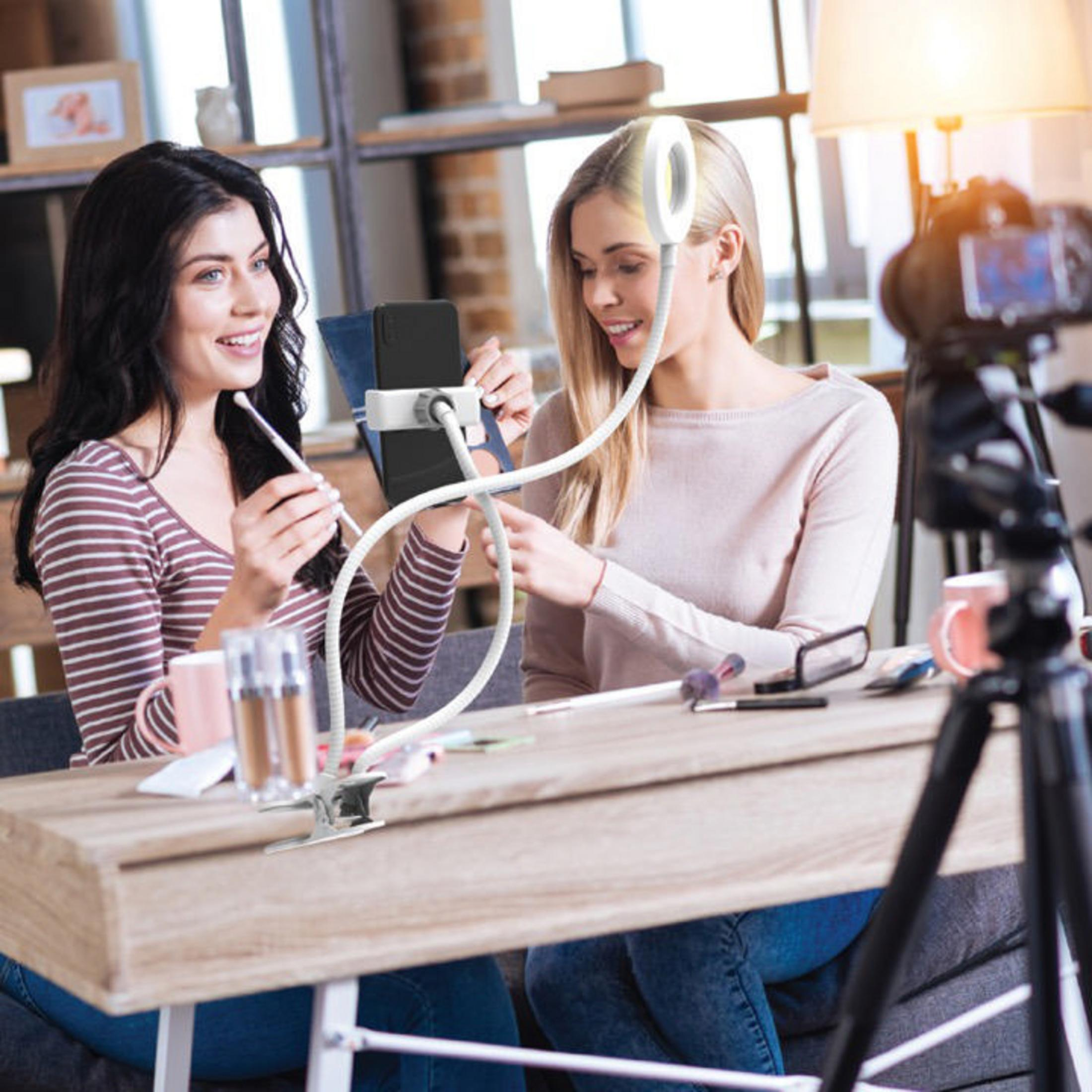 Dwie kobiety nagrywają film. Jedna trzyma telefon, oświetlenie pierścieniowe i statyw w tle.