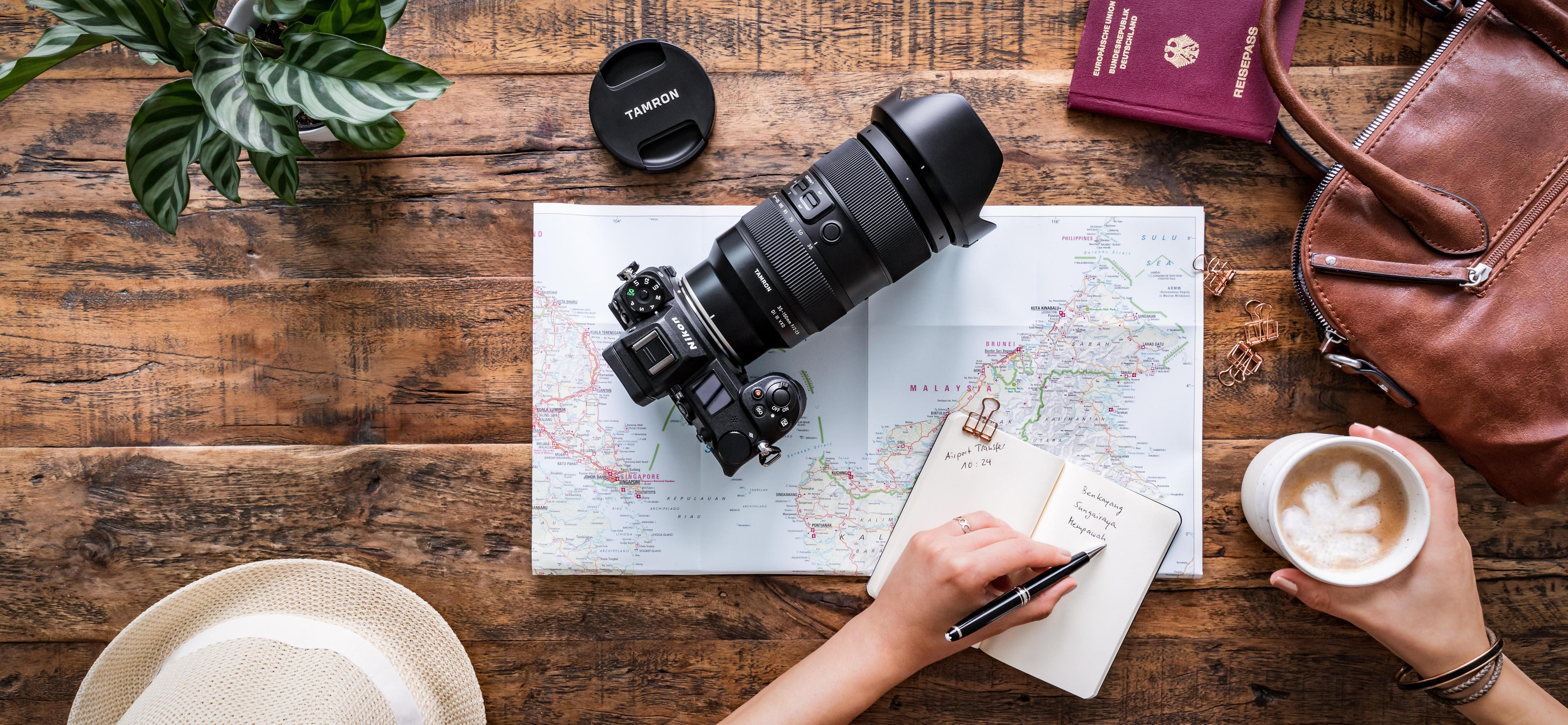 Aparat i obiektyw na mapie, z ręką piszącą w notatniku.