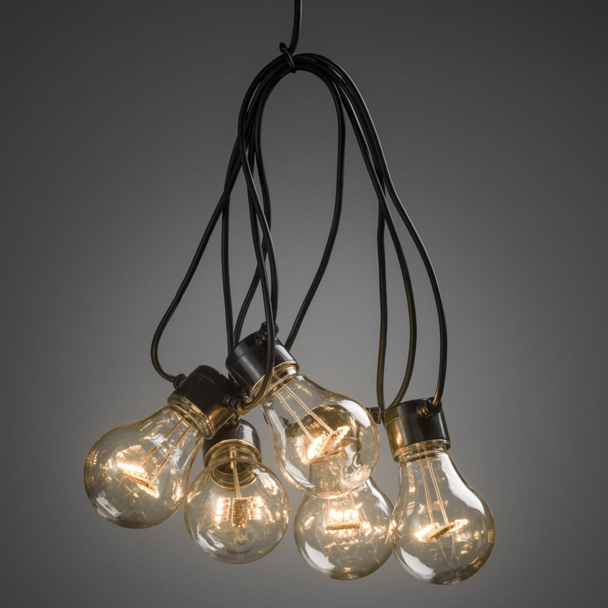 Eine Ansammlung von fünf Edison-Glühbirnen, die an schwarzen Kabeln hängen, auf grauem Hintergrund.