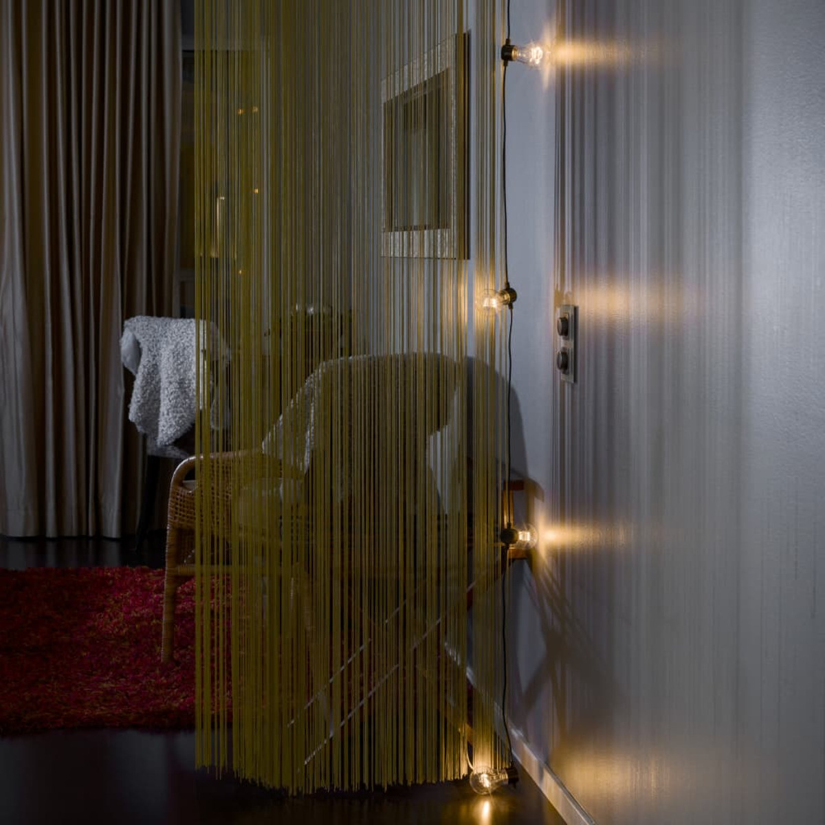 Ein Raum mit gelbem Vorhang, Stuhl und Lichterkette an der Wand.