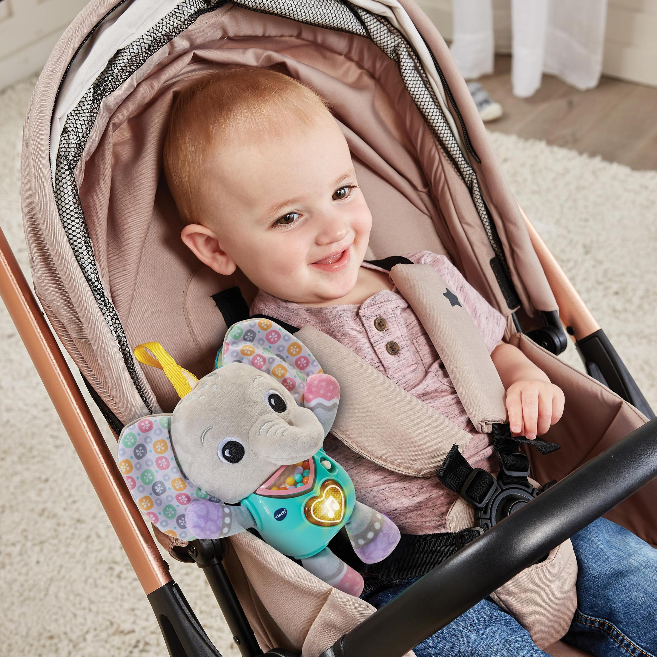Baby in einem Kinderwagen mit einem Spielzeug-Elefanten. Das Baby lächelt, mit rosa Decke.