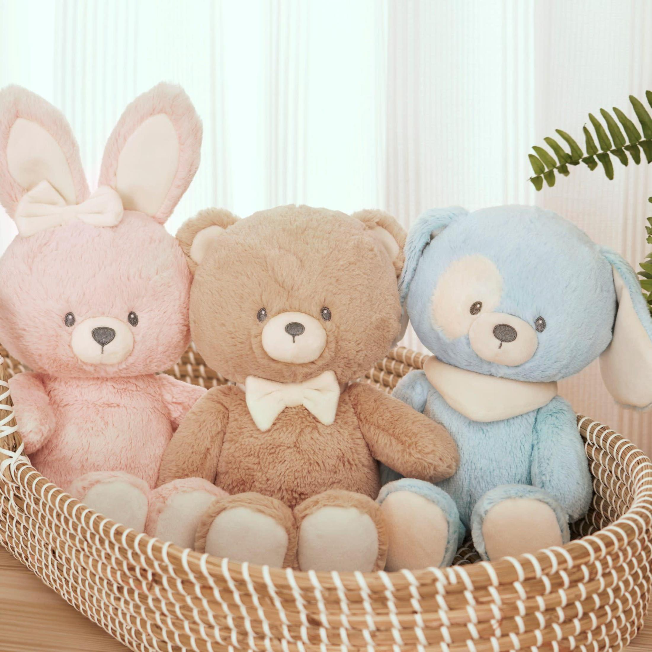 Drei Plüsch-Teddybären in einem Korb. Rosa Hase, brauner Bär und blauer Hund.