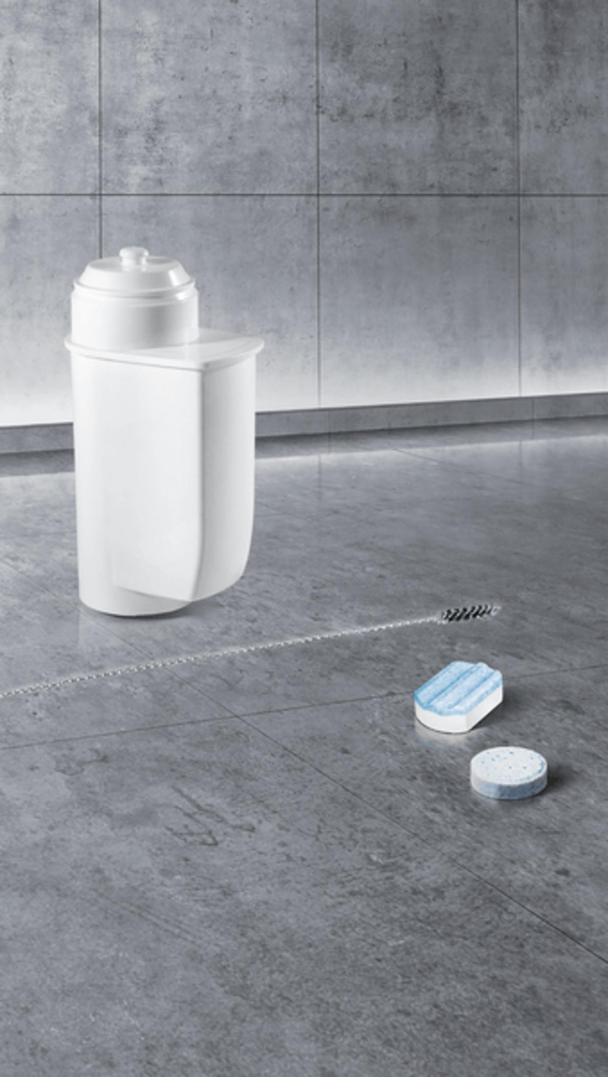 Filtro per l'acqua bianco con due pastiglie per la pulizia su un pavimento di piastrelle grigie.