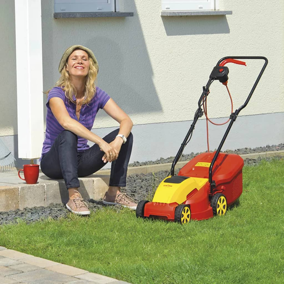 Eine Frau sitzt auf Stufen neben einem Rasenmäher, mit einer Tasse und Gras.