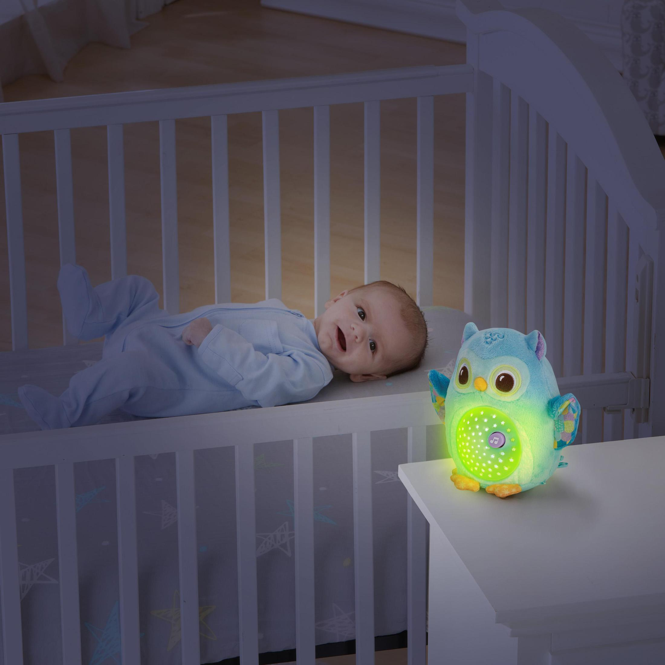 Ein Baby, das in einem Kinderbett lächelt, mit einem leuchtenden eulenartigen Nachtlicht.