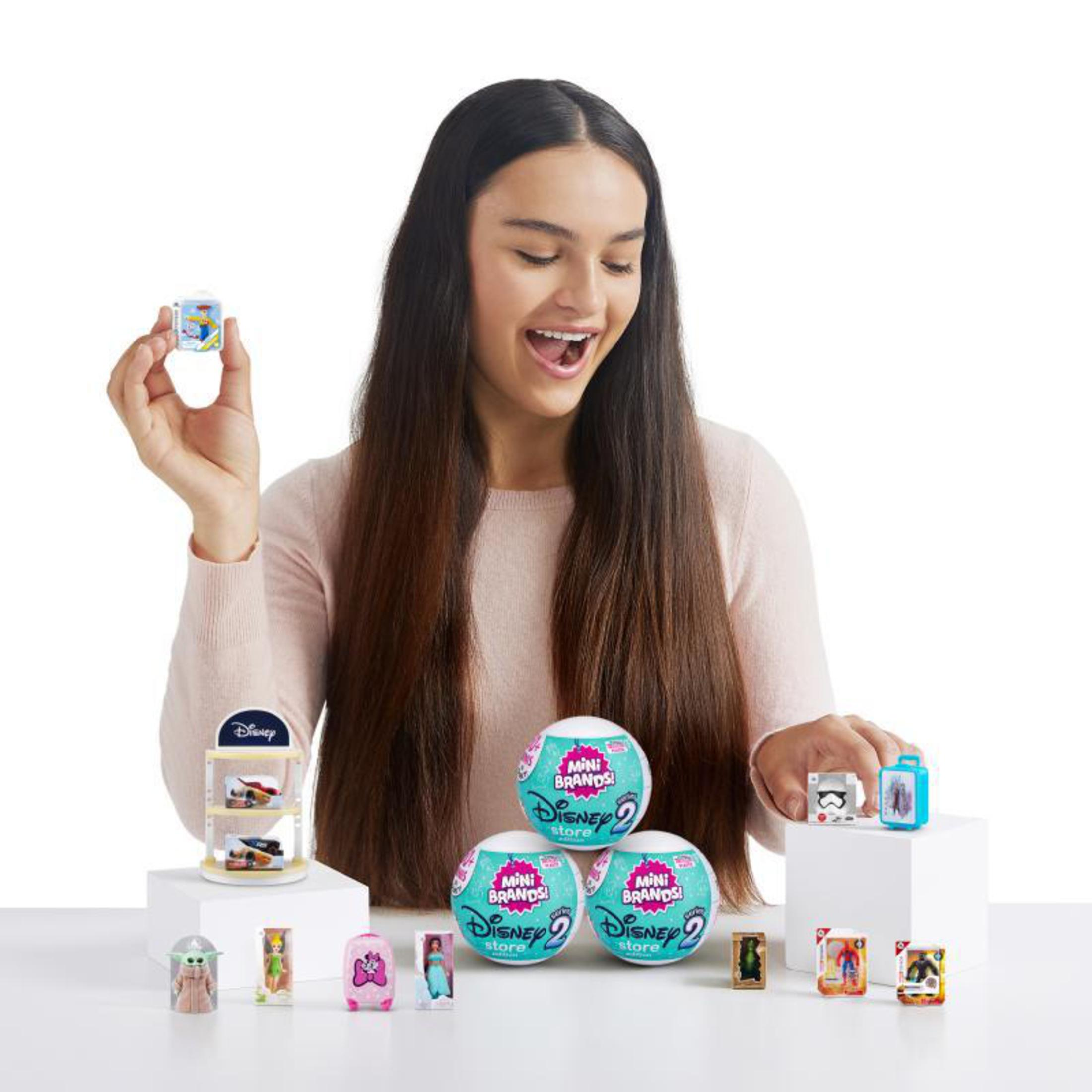 Eine lächelnde Frau mit Mini-Disney-Store-Spielzeugen. Spielzeuge befinden sich in Ausstellungsboxen und in durchsichtigen Plastikkugeln.