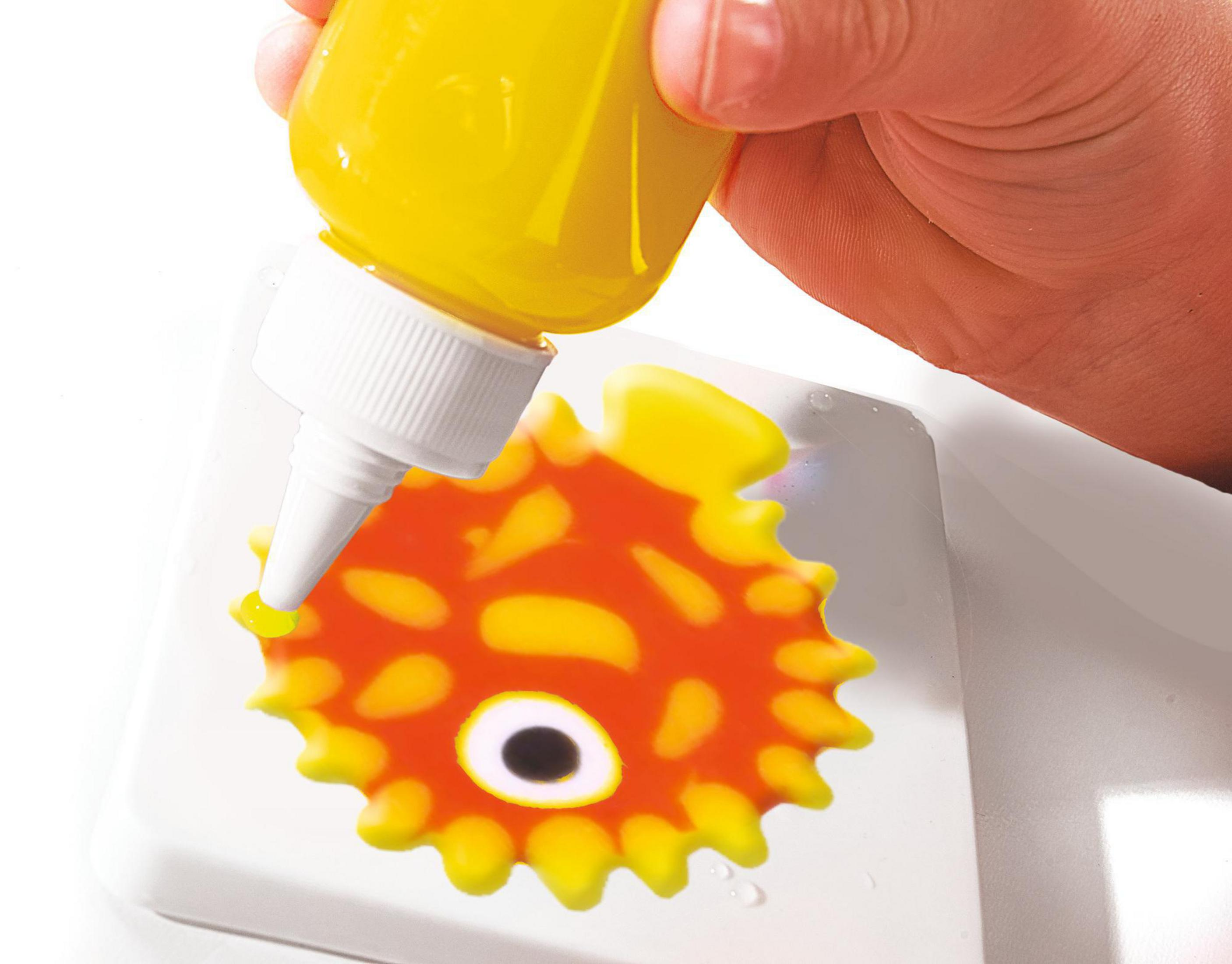 Hand gießt gelbe Flüssigkeit aus einer Flasche auf ein rot-gelbes Spielzeug. Weißer Hintergrund.