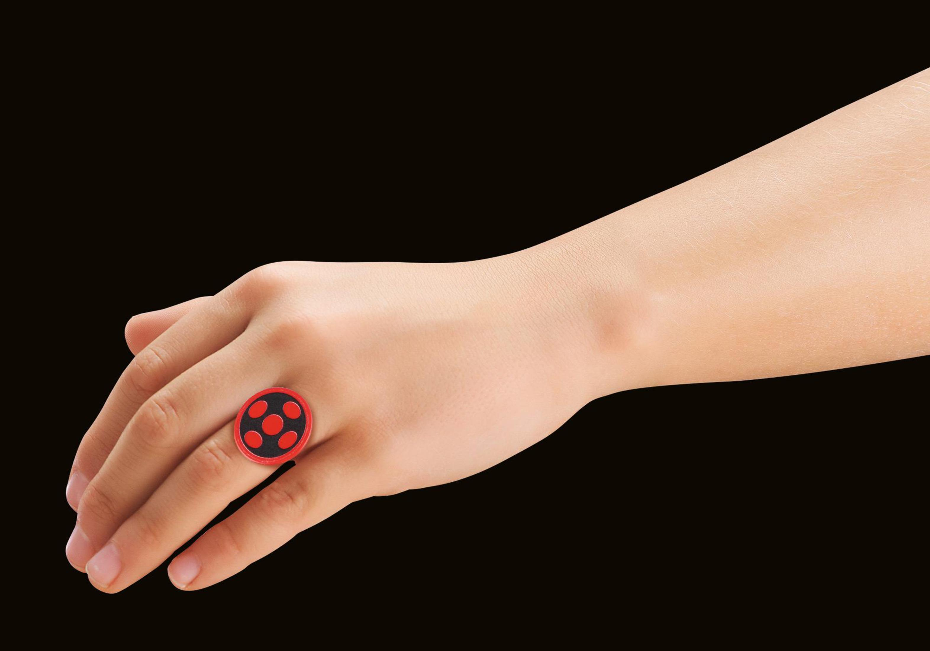 Eine Hand, die einen schwarz-roten Ring mit kreisförmigem Design trägt. Der Hintergrund ist dunkel.