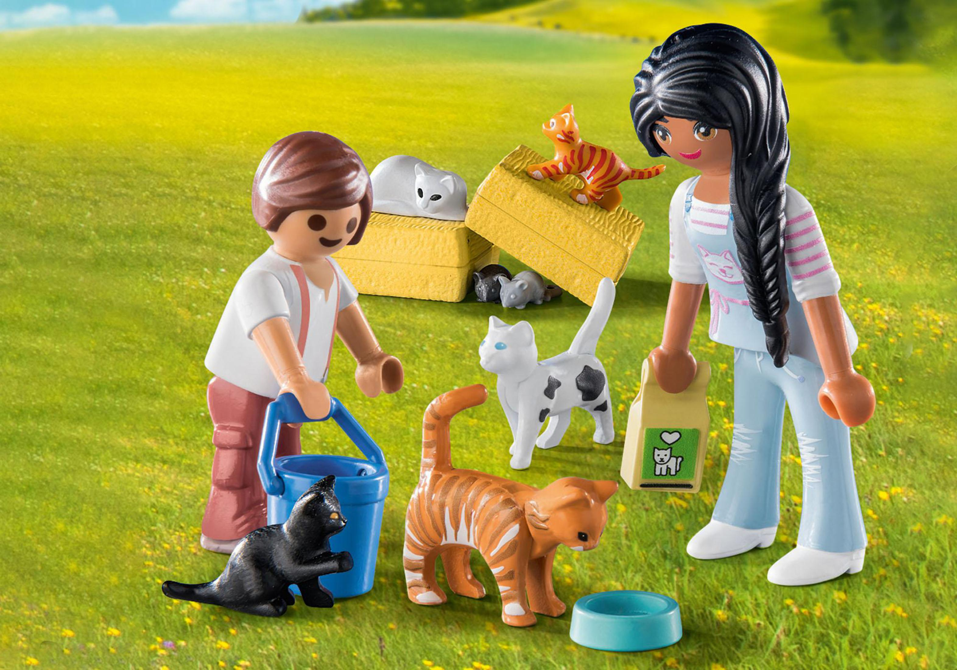 Playmobil-Figuren füttern Katzen auf einer Wiese mit Heuballen und einer blauen Futterschale.