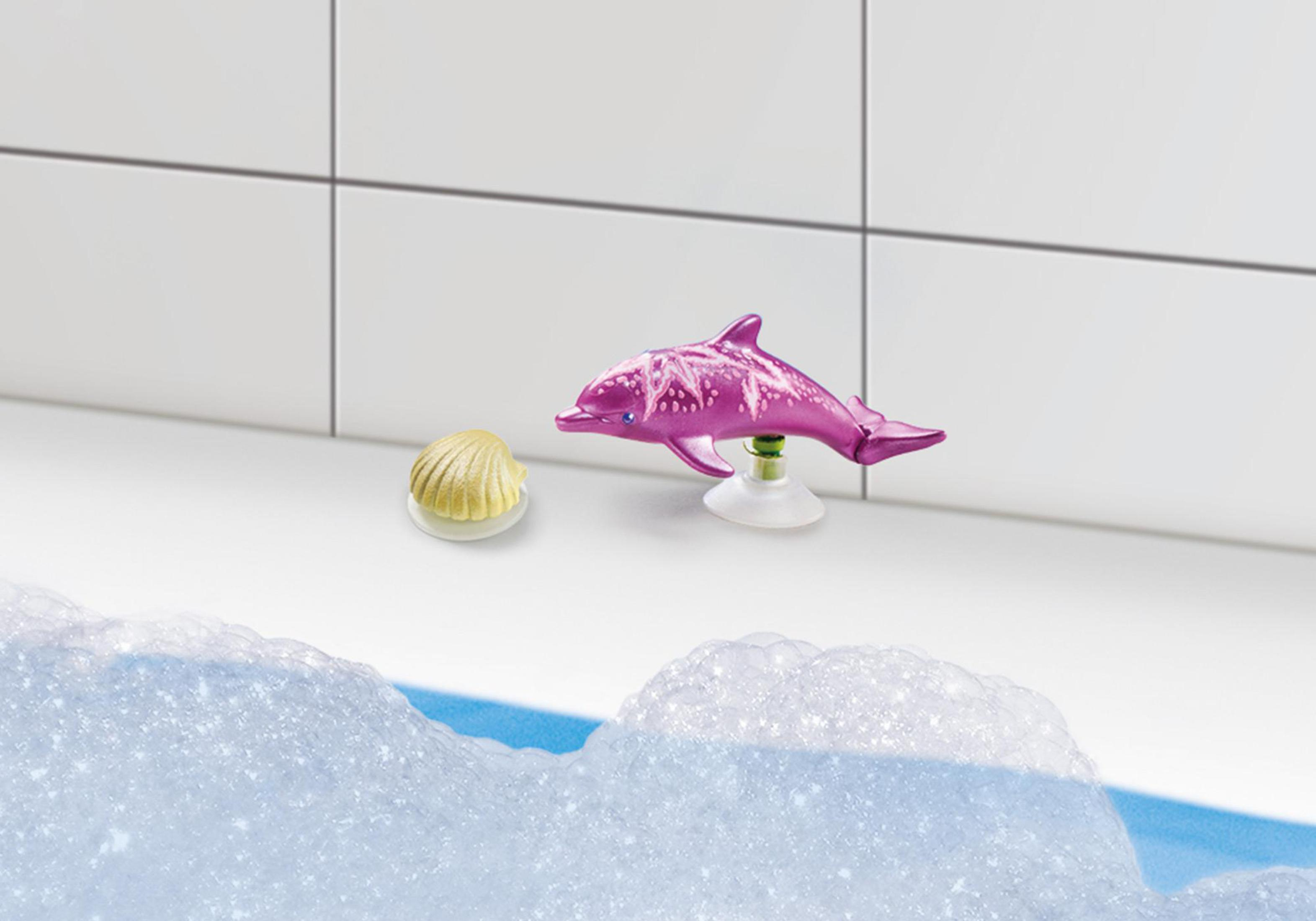 Spielzeugdelfin in einer Badewanne mit Blasen und einem Muscheltier auf weißer Oberfläche.