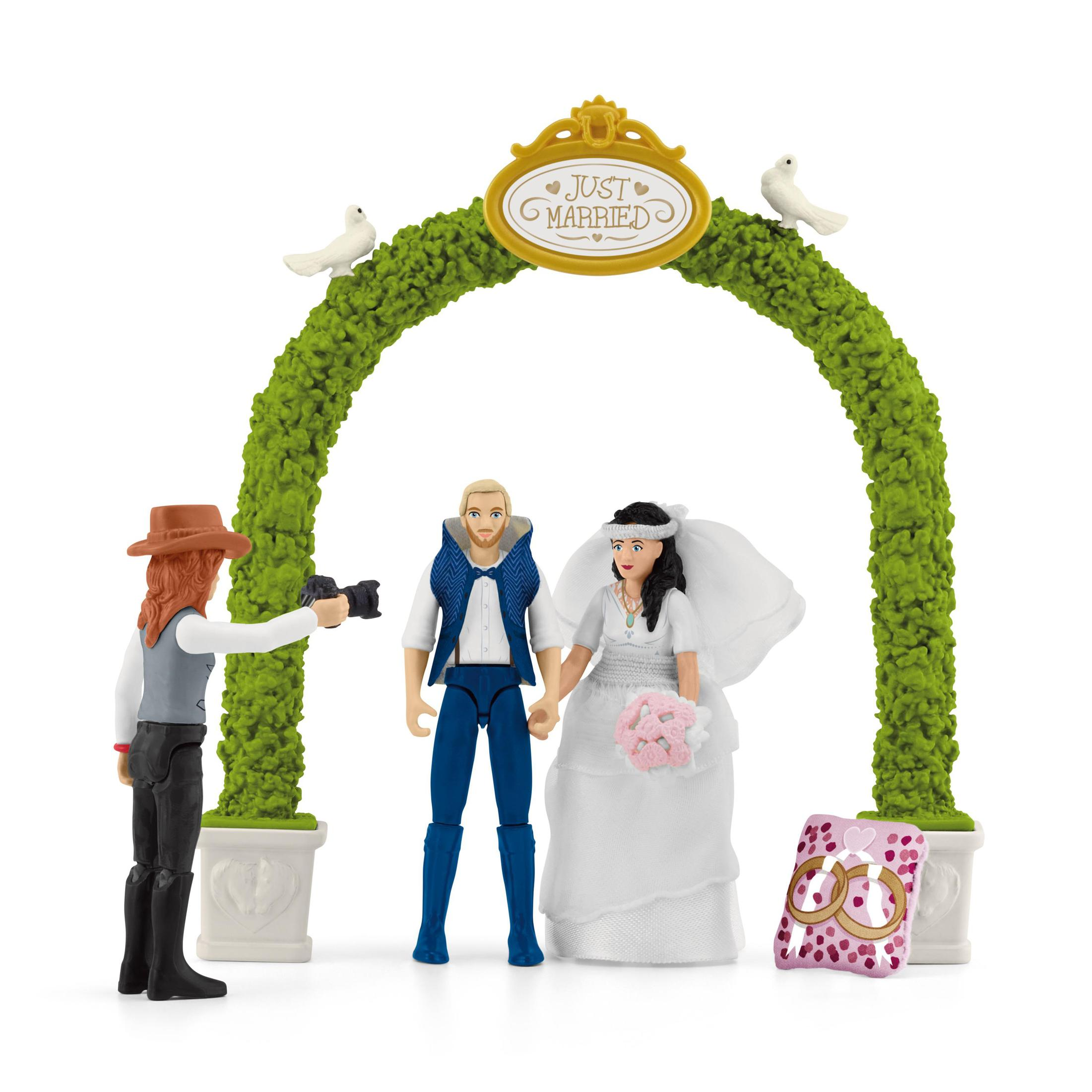 Toy wedding scene. Bride and groom under an arch. Photographer taking a photo. White background.